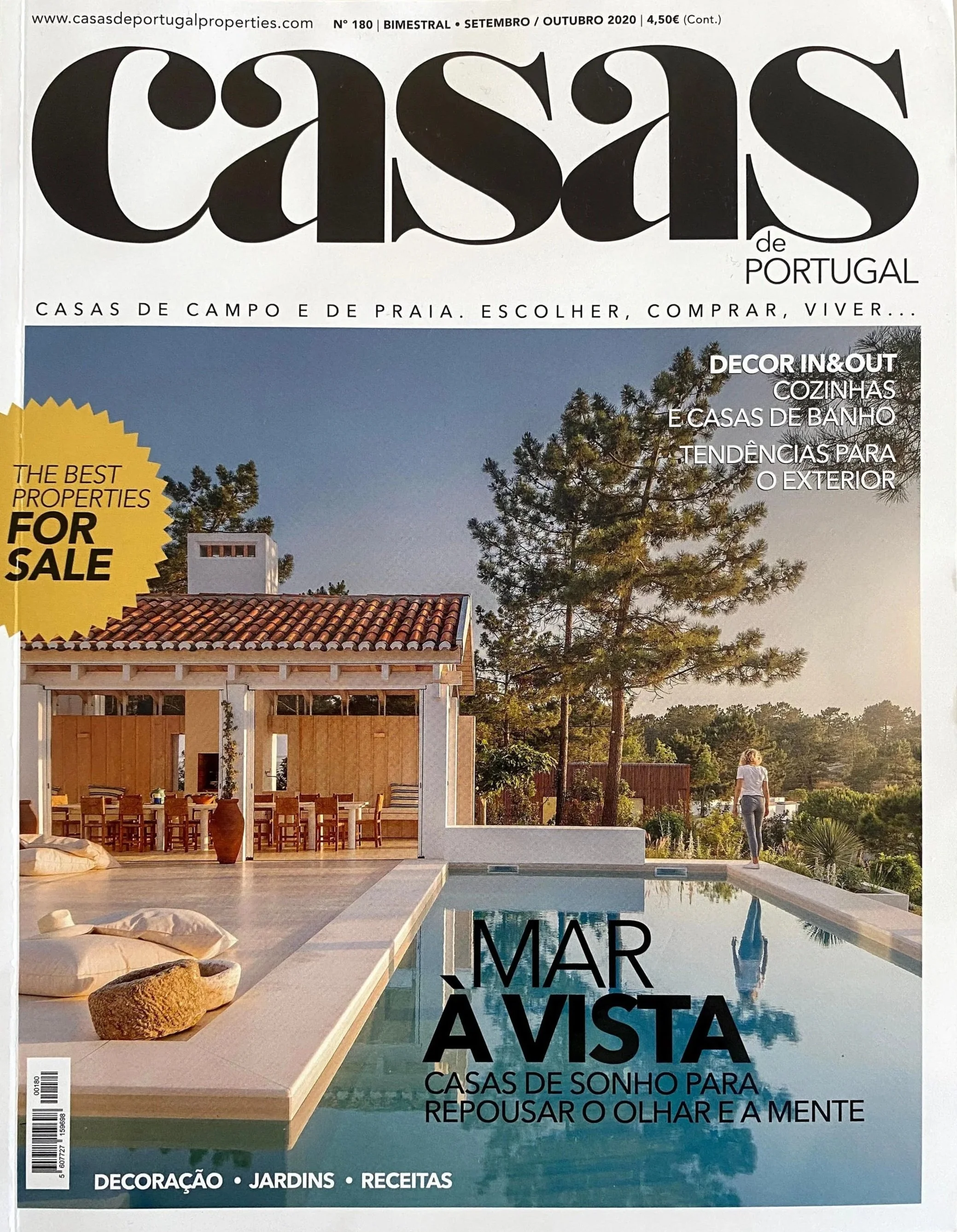 Cover of a magazine titled 'Casas de Portugal' featuring a modern house with a swimming pool, outdoor dining area, and a woman standing near the pool under a clear sky.