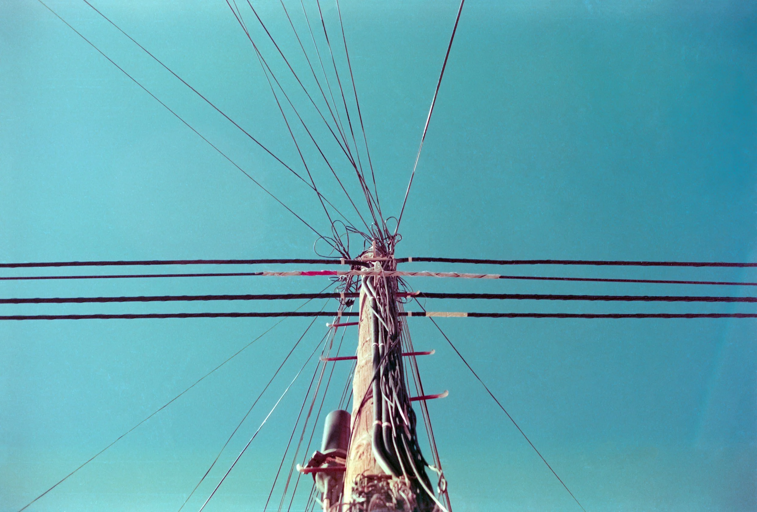 The image shows an upward view of a power pole with multiple power lines extending from it and a clear blue sky in the background.