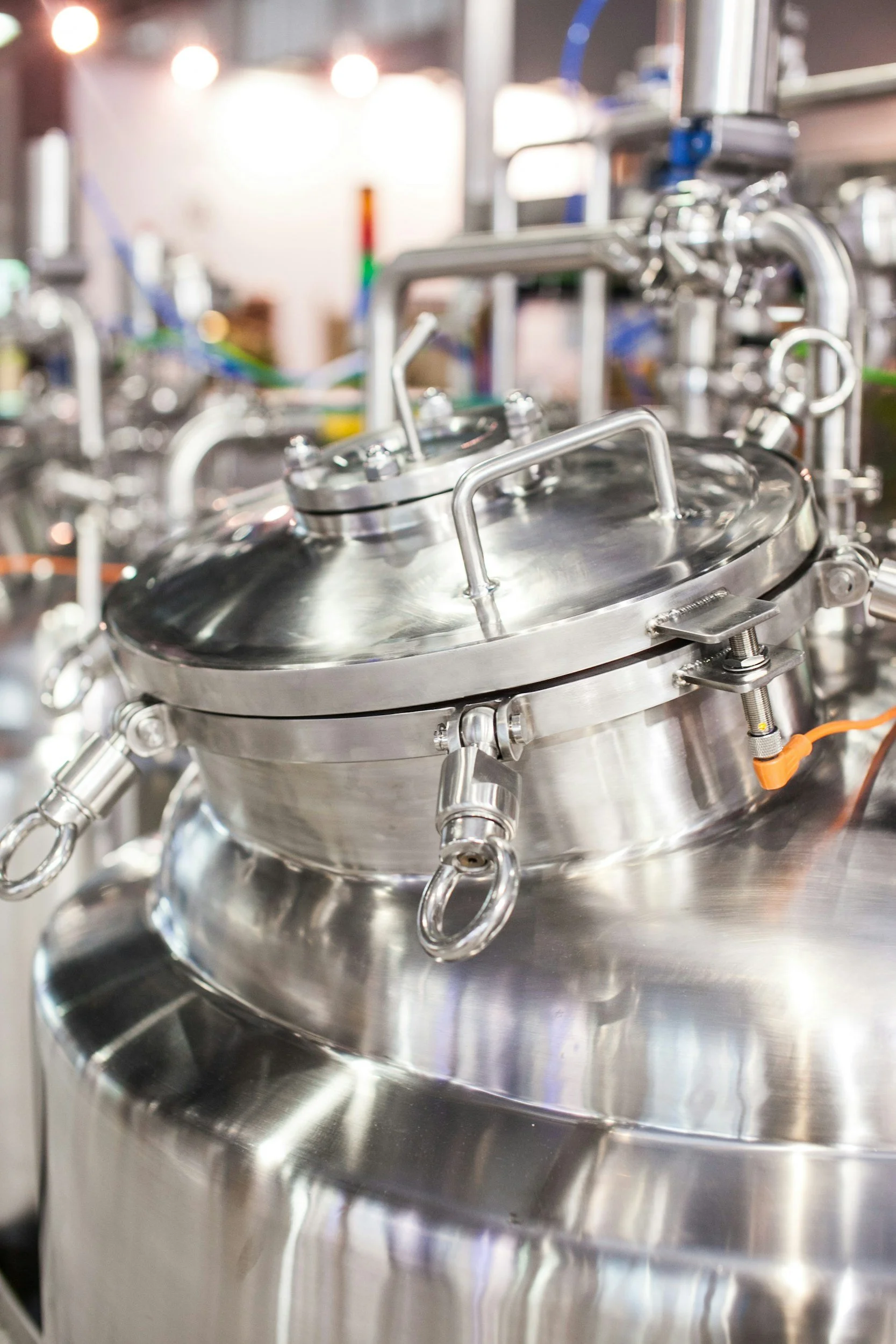 Close-up of a stainless steel chemical reactor with a lid and various pipes and fittings.