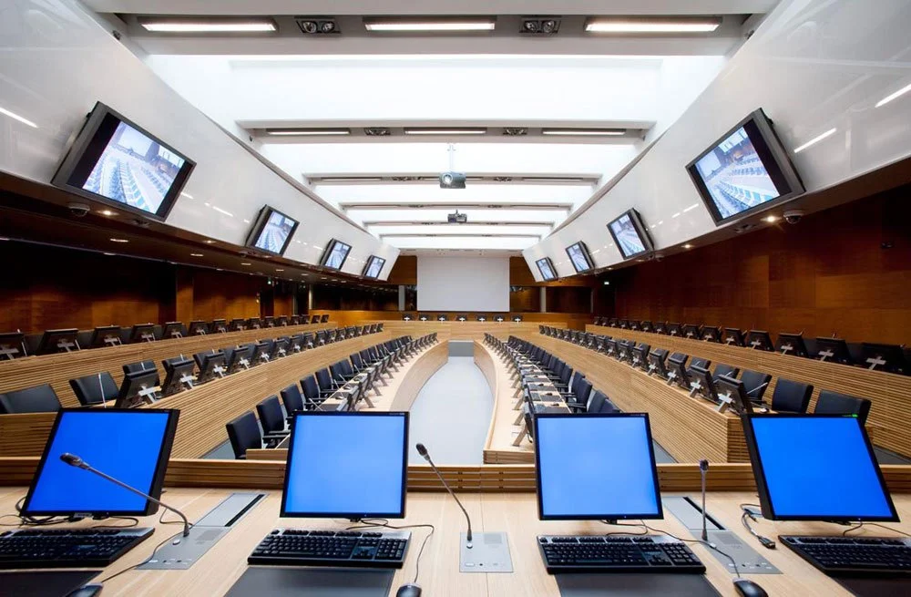 Empty conference room with rows of chairs, a large screen at the front, multiple computer monitors on desks, and multiple television screens mounted on the walls.
