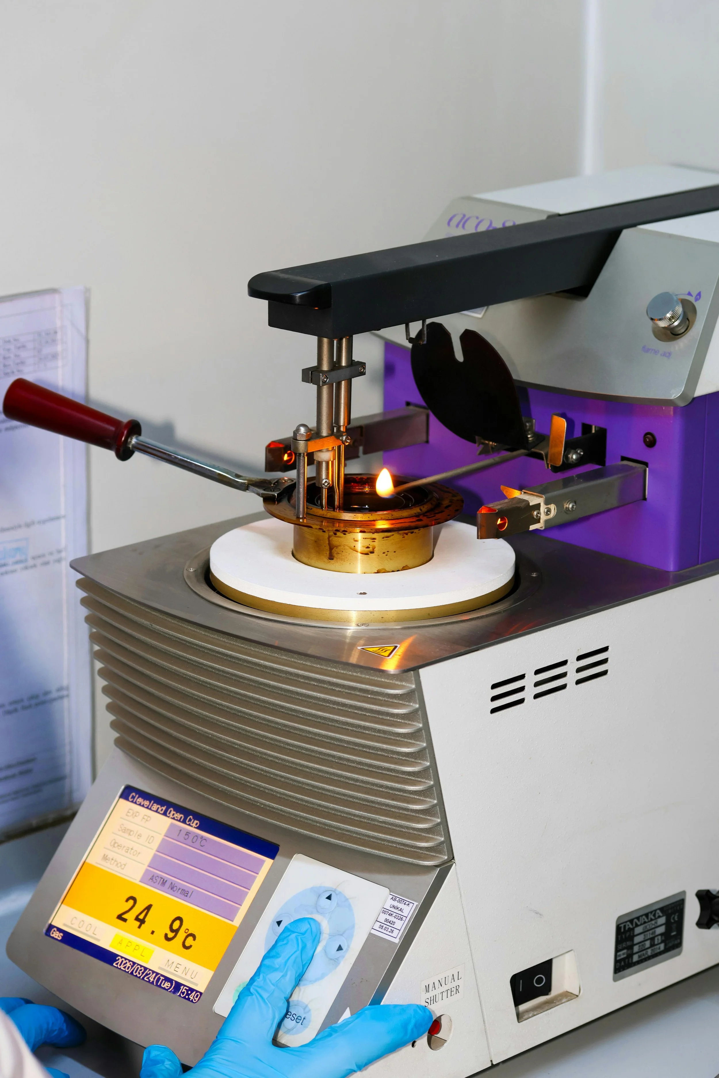 Laboratory scientist wearing blue gloves using a machine with a digital screen displaying temperature 24.9°C, on a laboratory countertop.