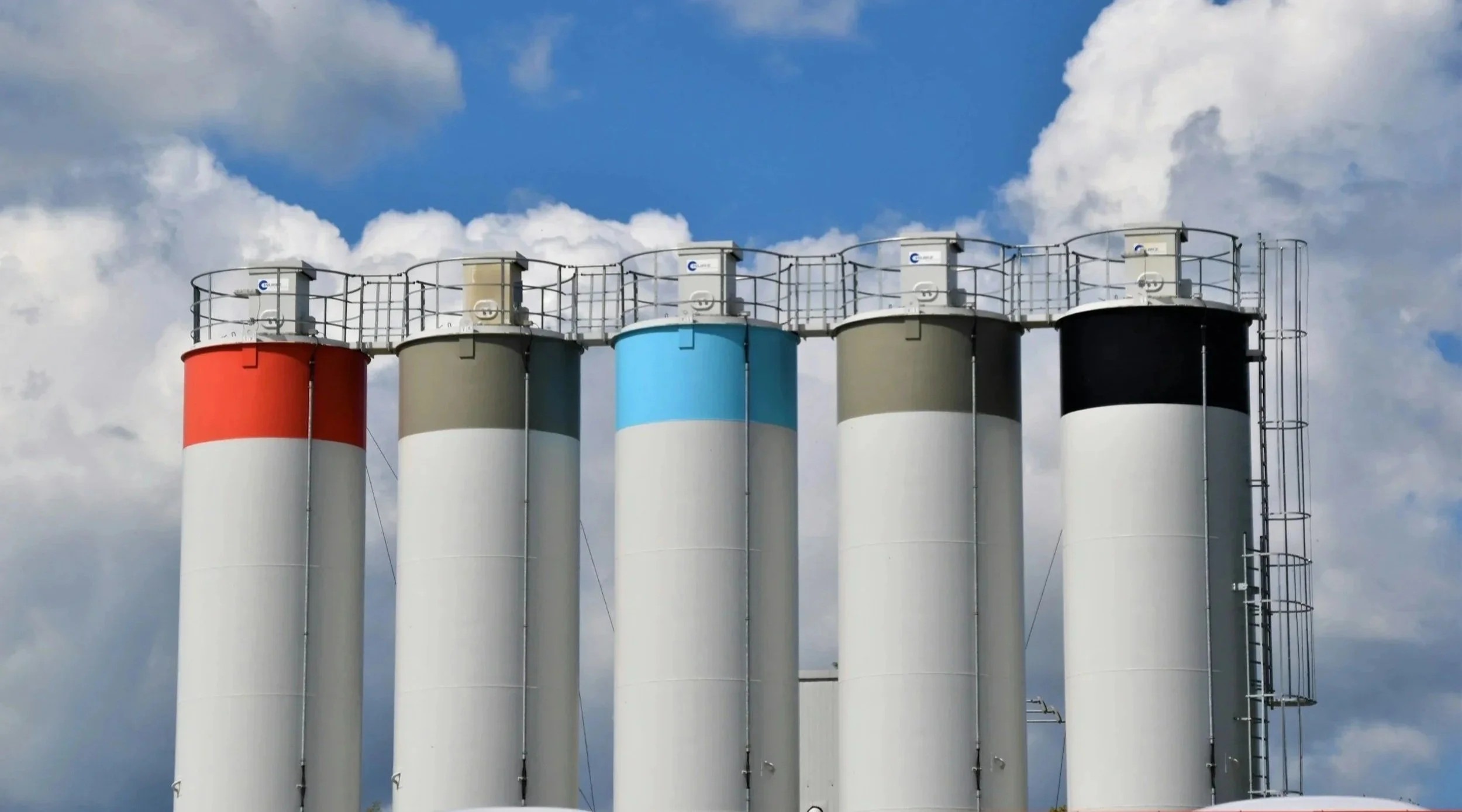 Five vertical chemical bulk storage tanks with a cloudy sky in the background