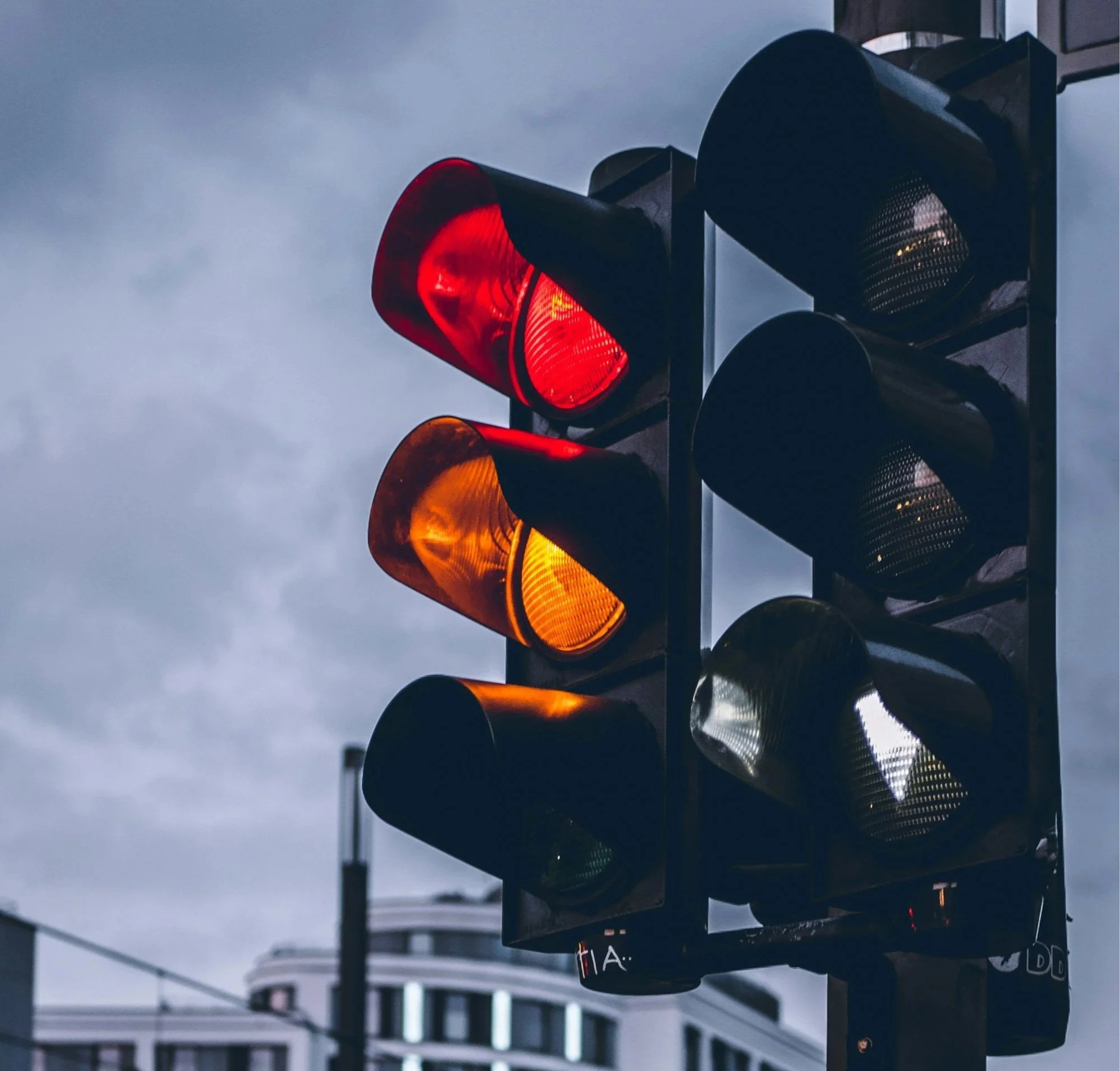 Traffic light showing a red light against a cloudy sky background.