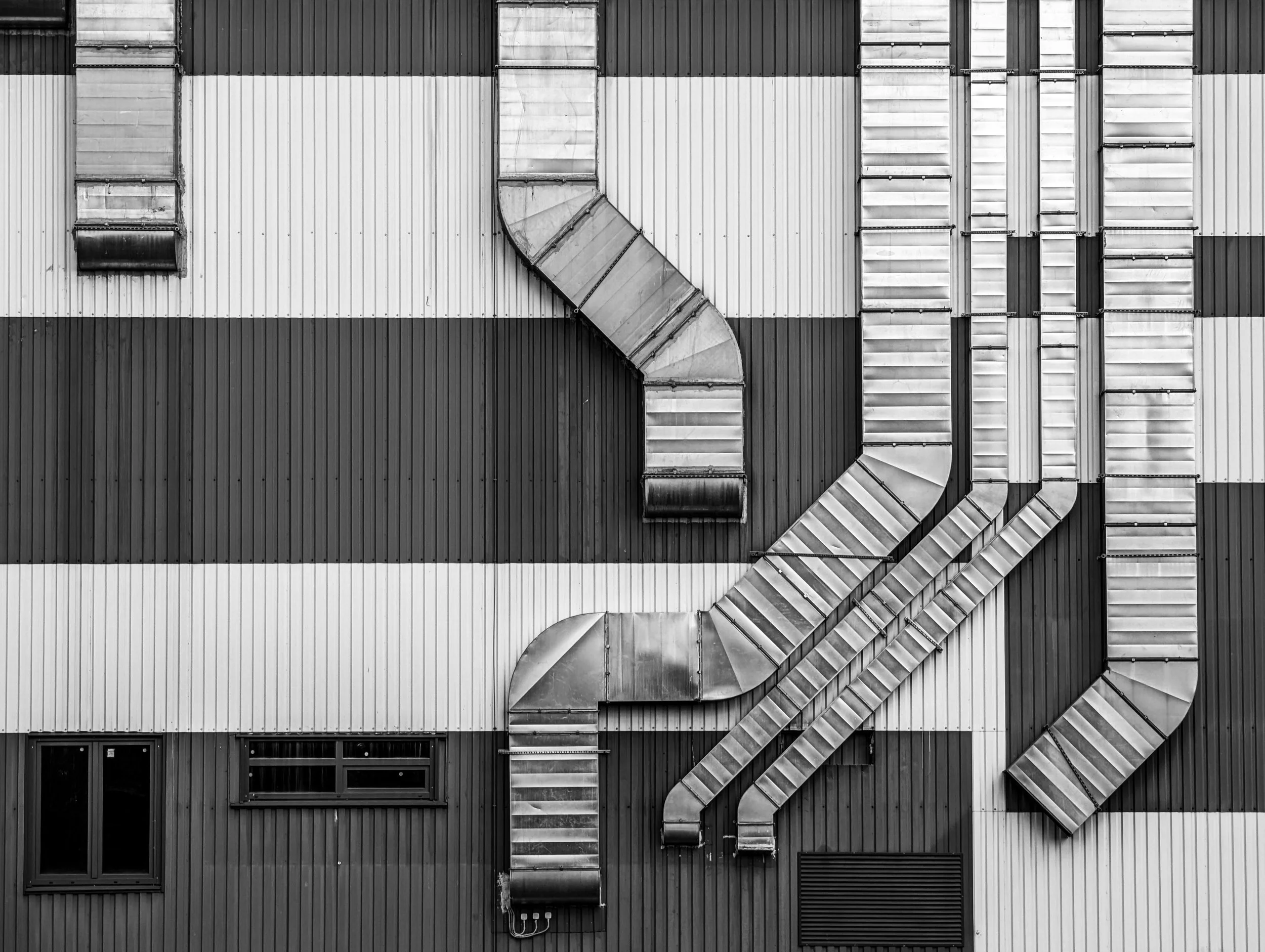 Black and white photo of a building's exterior with multiple metal ventilation ducts arranged vertically against a striped wall.