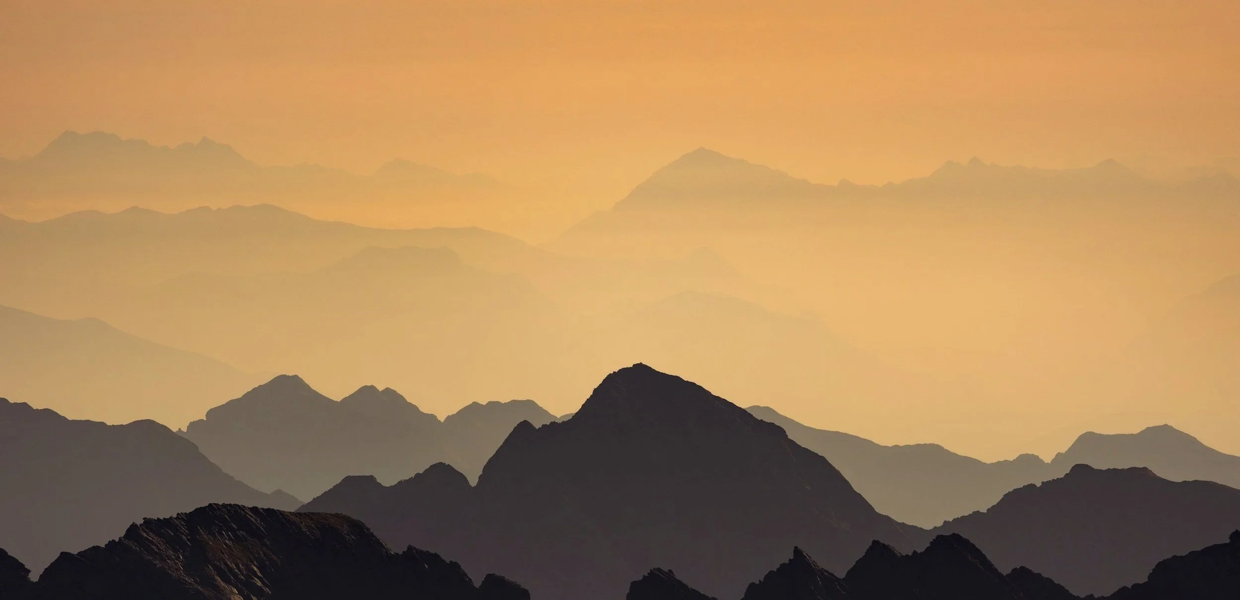 Silhouettes of mountain peaks at sunset with a yellow-orange sky.