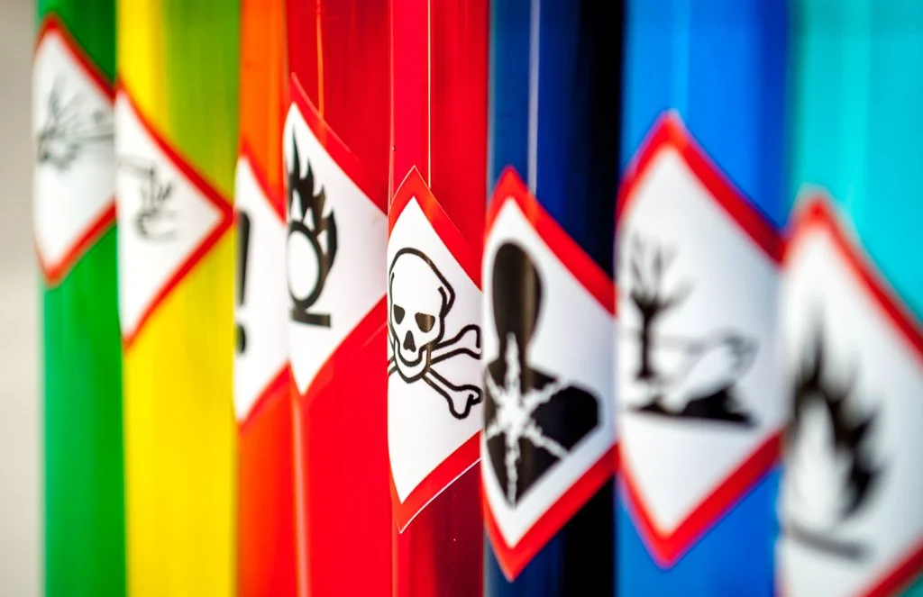 Colorful barrels with hazardous material warning labels, including skull and crossbones and flame symbols.