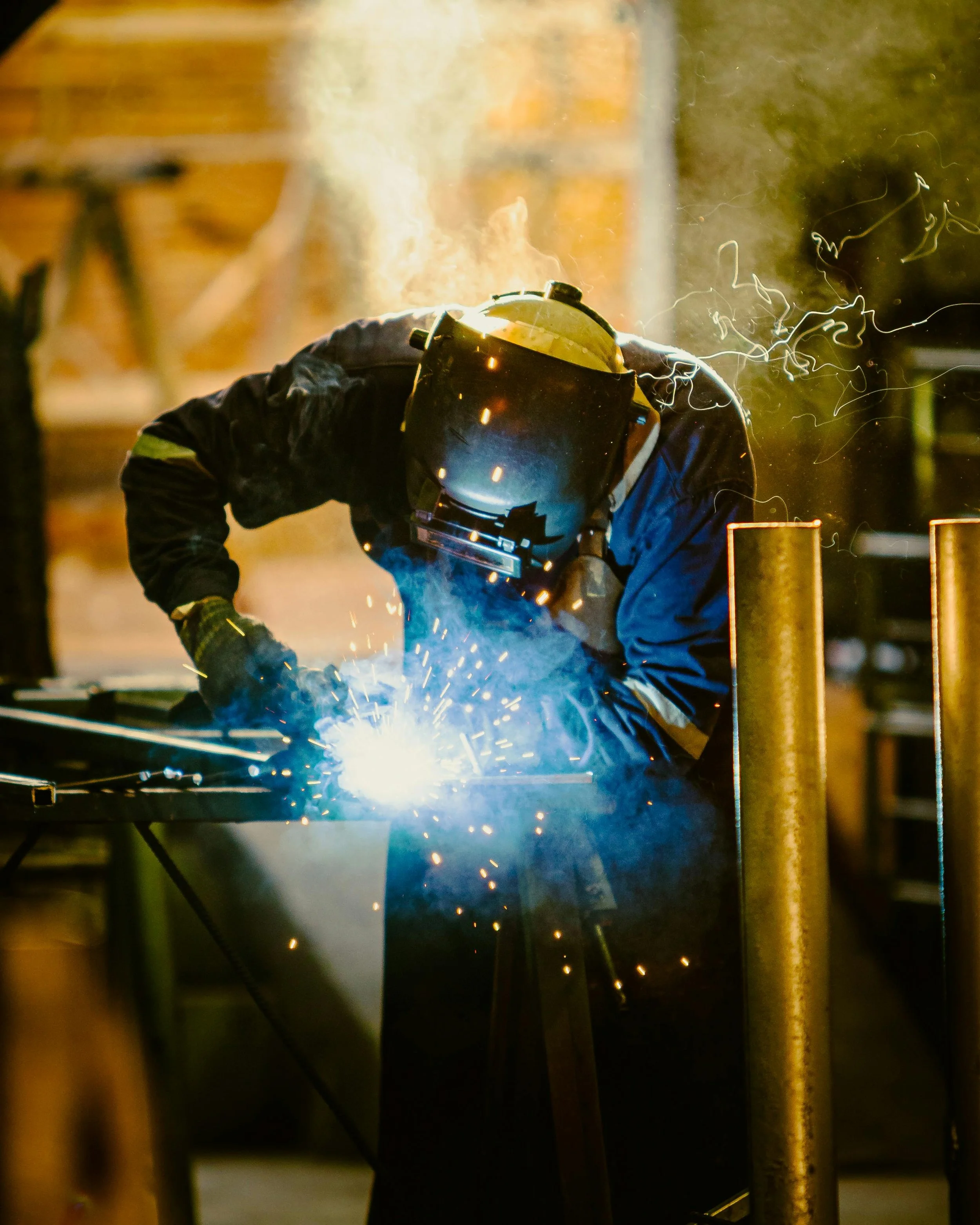 A person welding metal with sparks and bright light in a workshop or industrial setting.