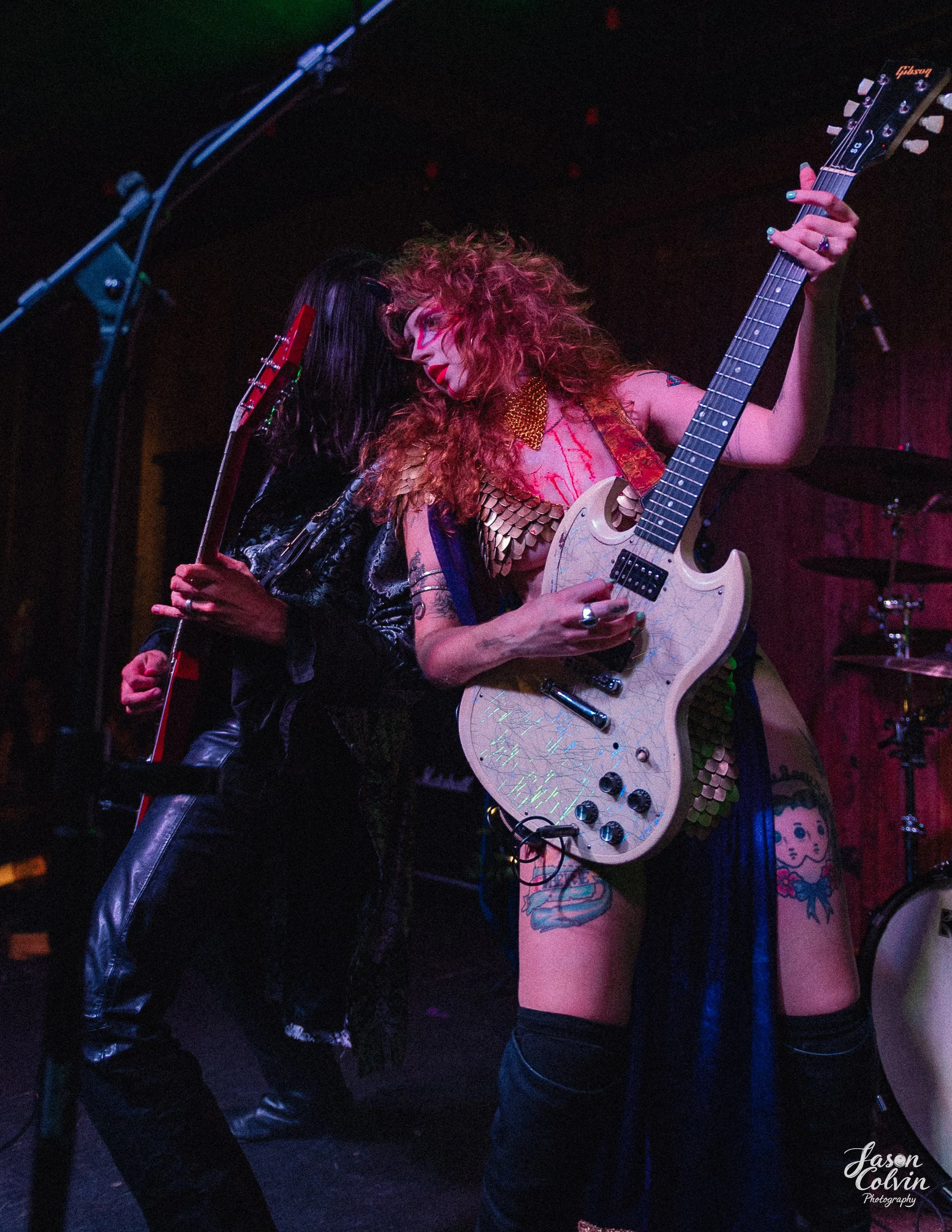Two female musicians playing electric guitars on stage during a concert.