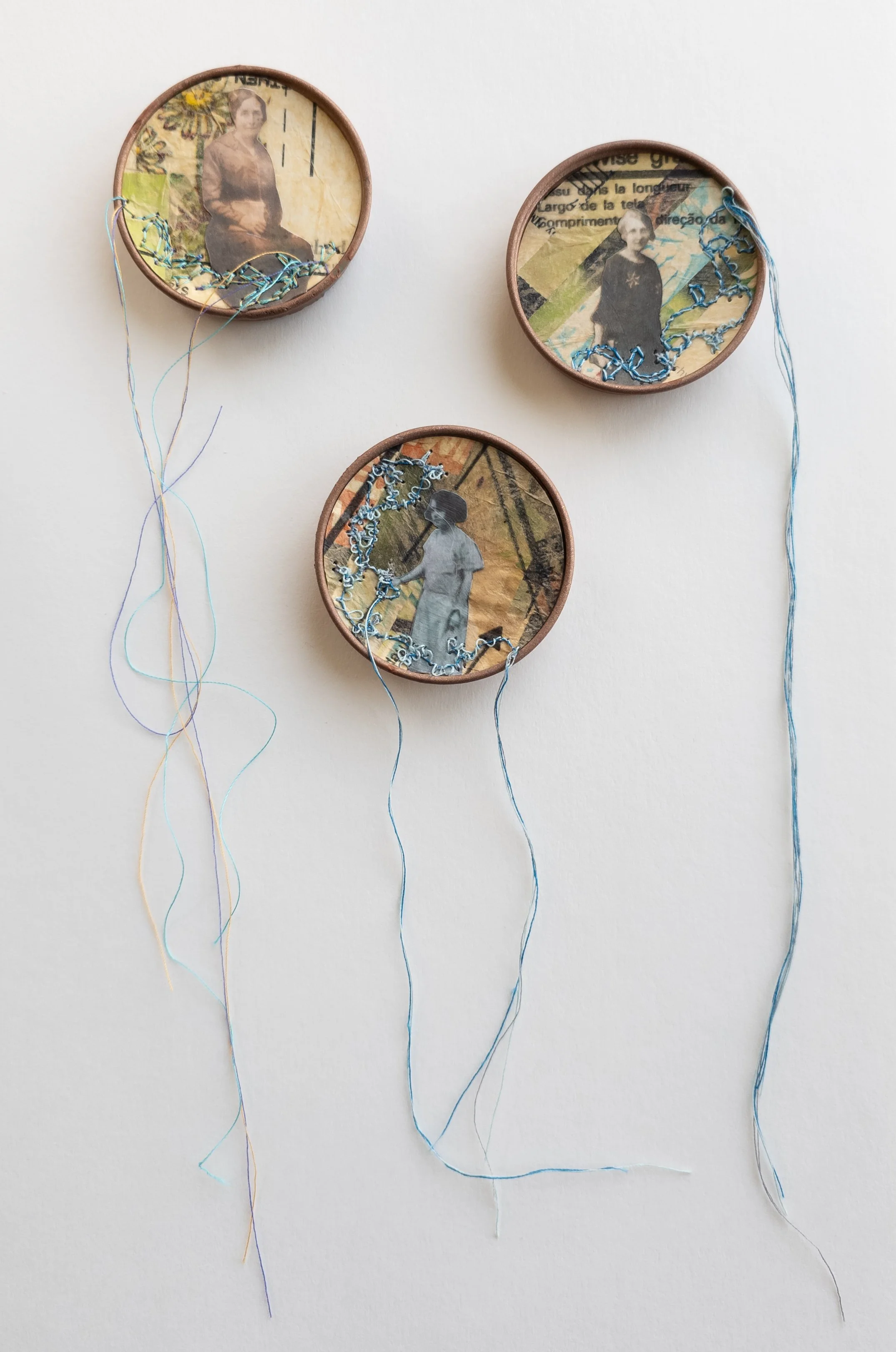  Mothers and Daughters Grouping No.3  
Mixed Media paper collage  

three 2" babyfood jar lids frame these 2" pieces with thread suspended 6 to 9"" below   