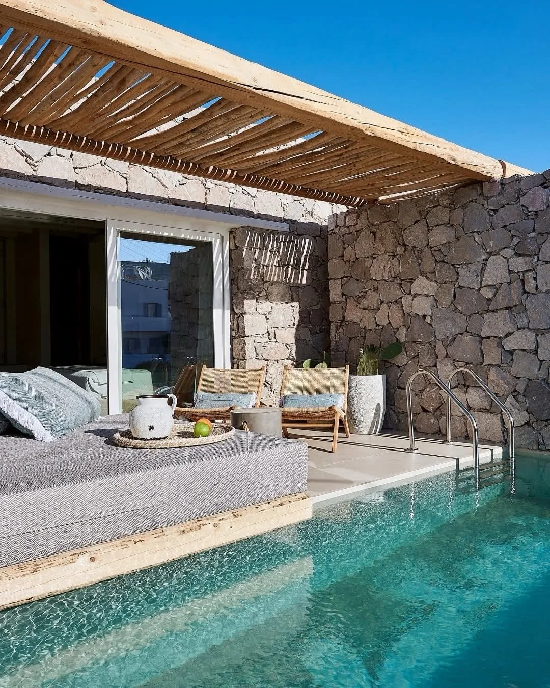 Luxurious hotel swimming pool area with lounge chairs and umbrellas, surrounded by modern buildings and palm trees, during sunset.