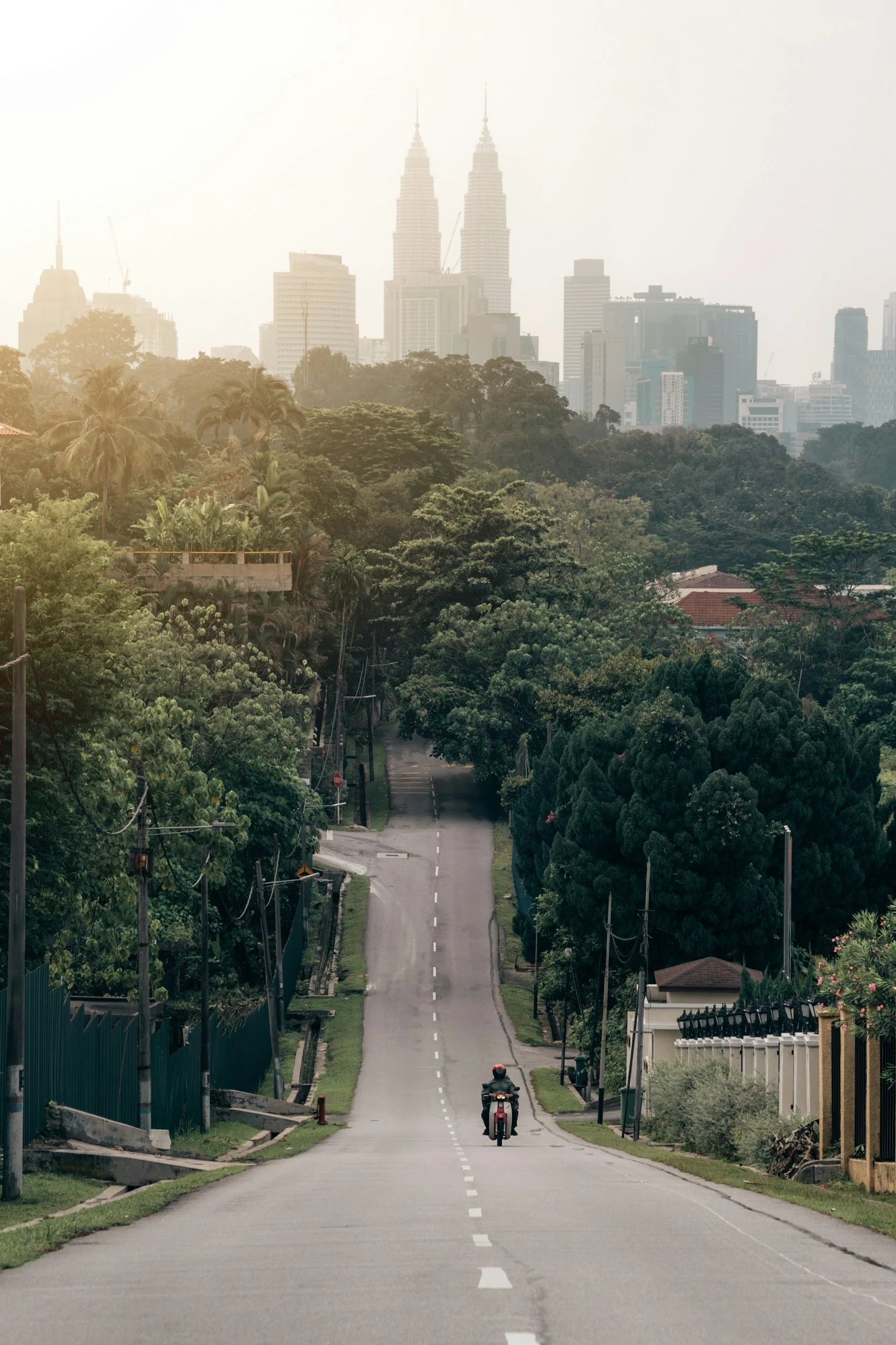 motorcyclist going up a hill with kuala lumpur skyline behind at sunset