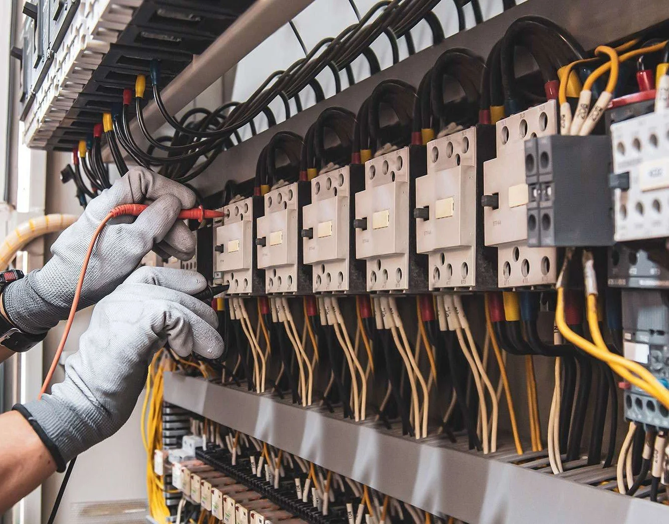 Technician wearing gray gloves working on an electrical circuit board with wires and relays.