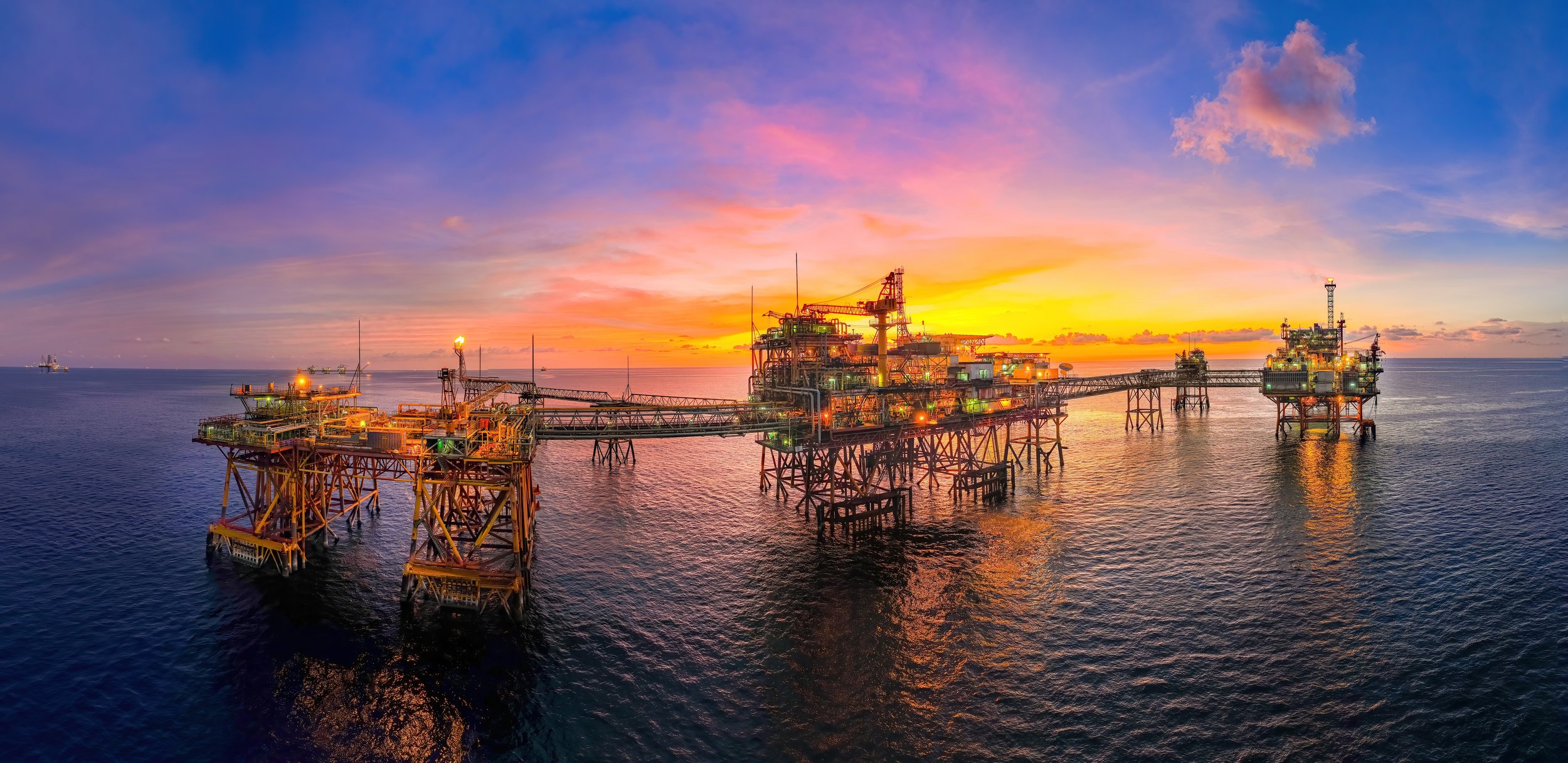 Offshore oil drilling platform at sunset over the ocean.