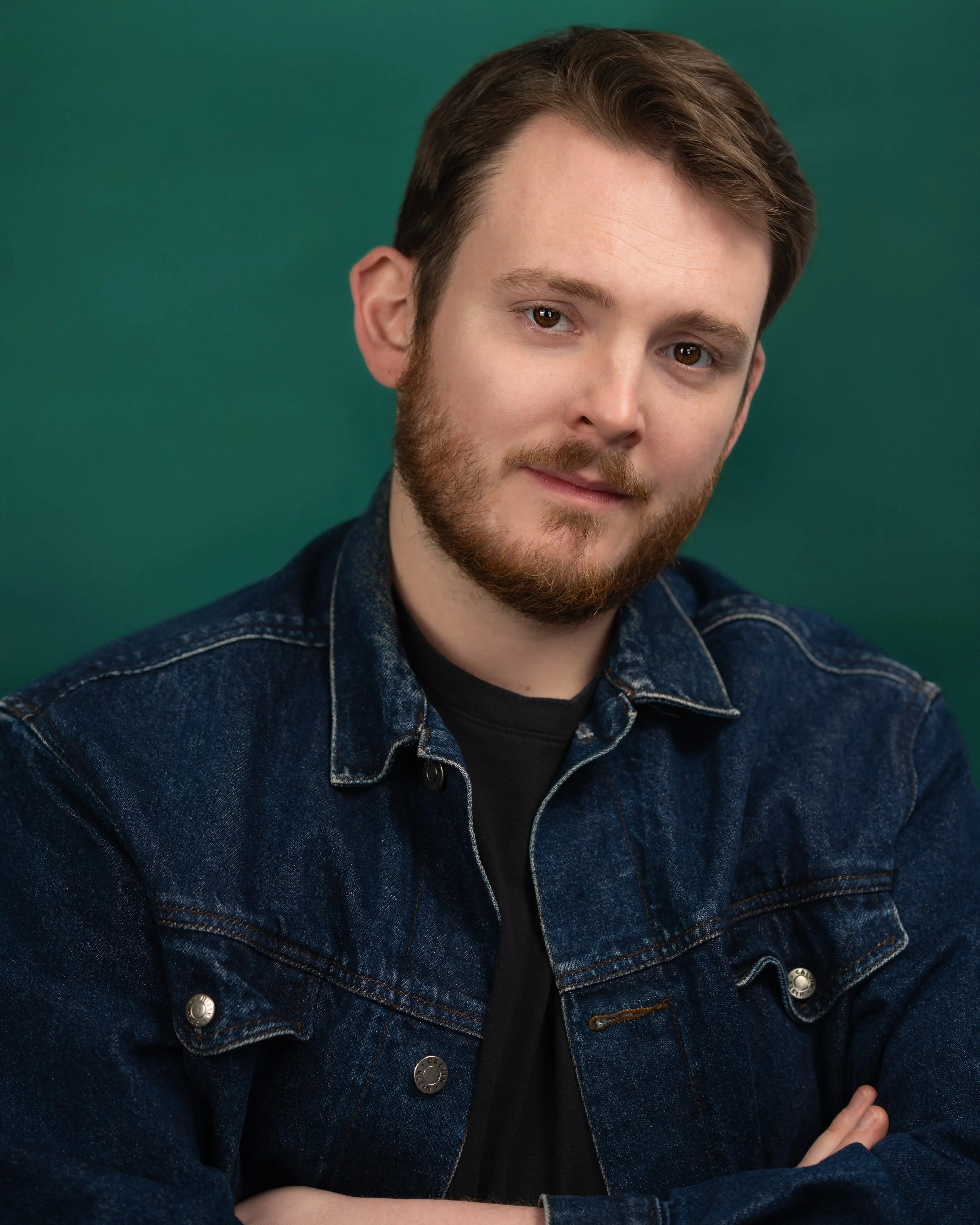 A headshot of Ronan Melomo in a denim jacket on a green background.