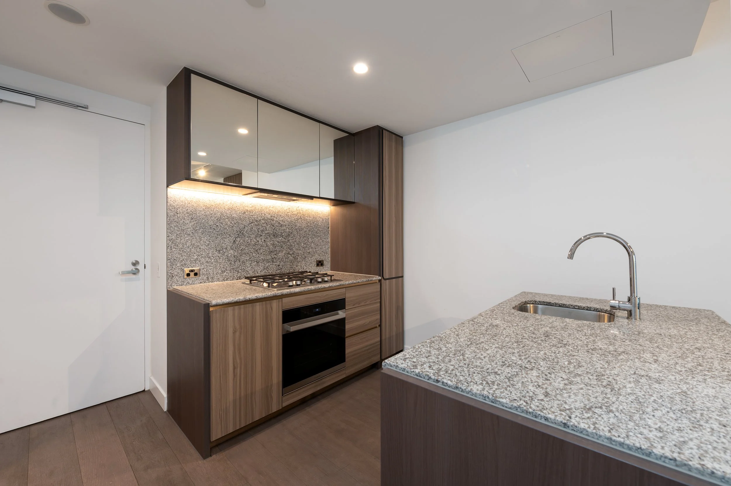 Modern kitchen with wood cabinets, granite countertops, built-in gas cooktop, and sink with faucet on an island.