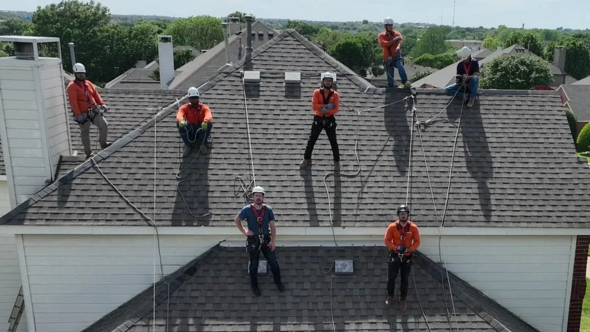 Roofing crew on house roof wearing safety harnesses.