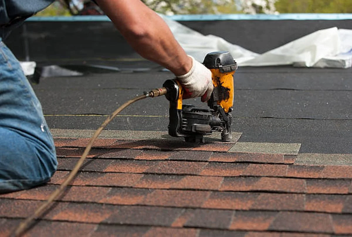 Roofer using nail gun on asphalt shingles.