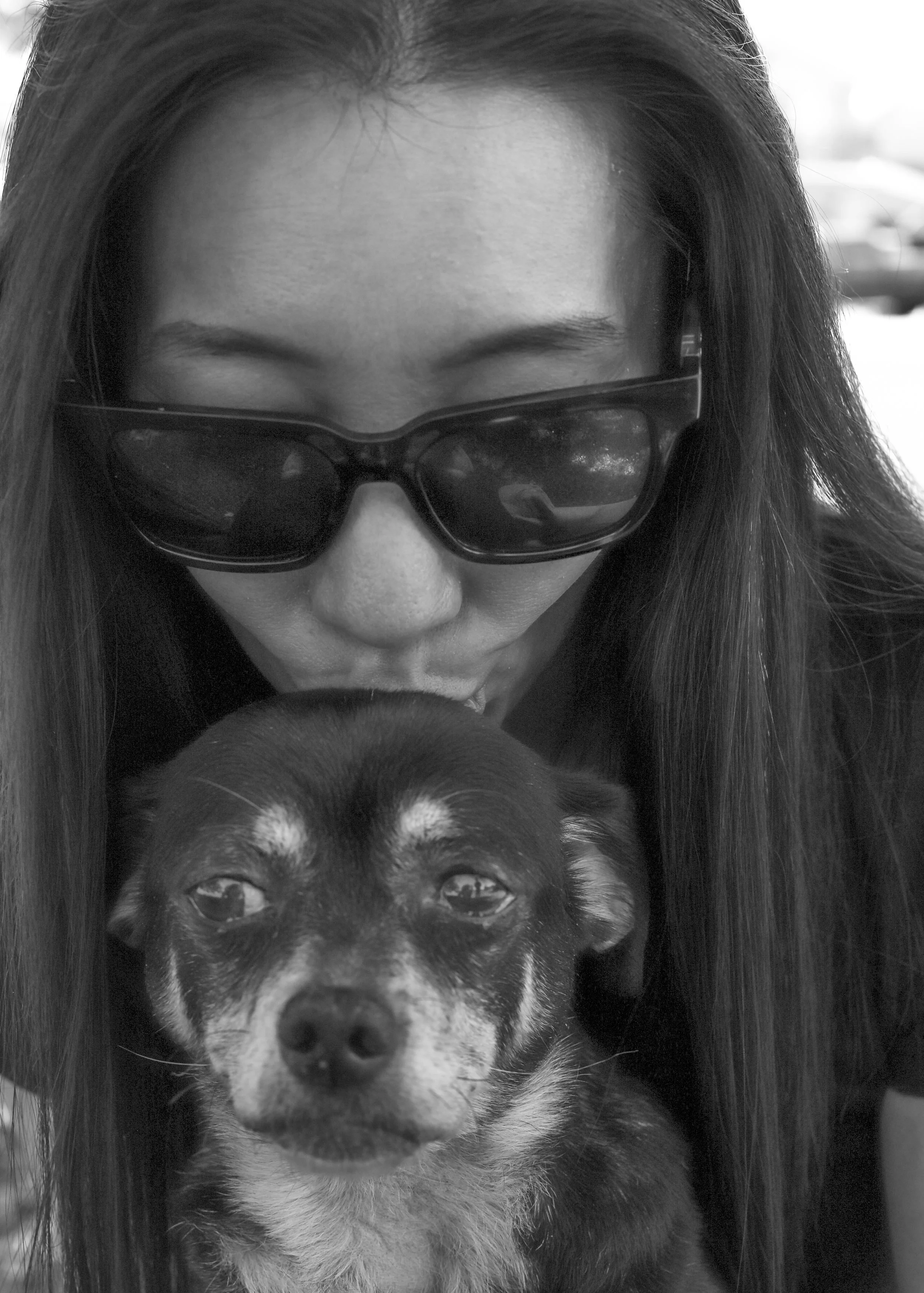 A woman wearing sunglasses kissing a small dog with a black and white fur pattern.