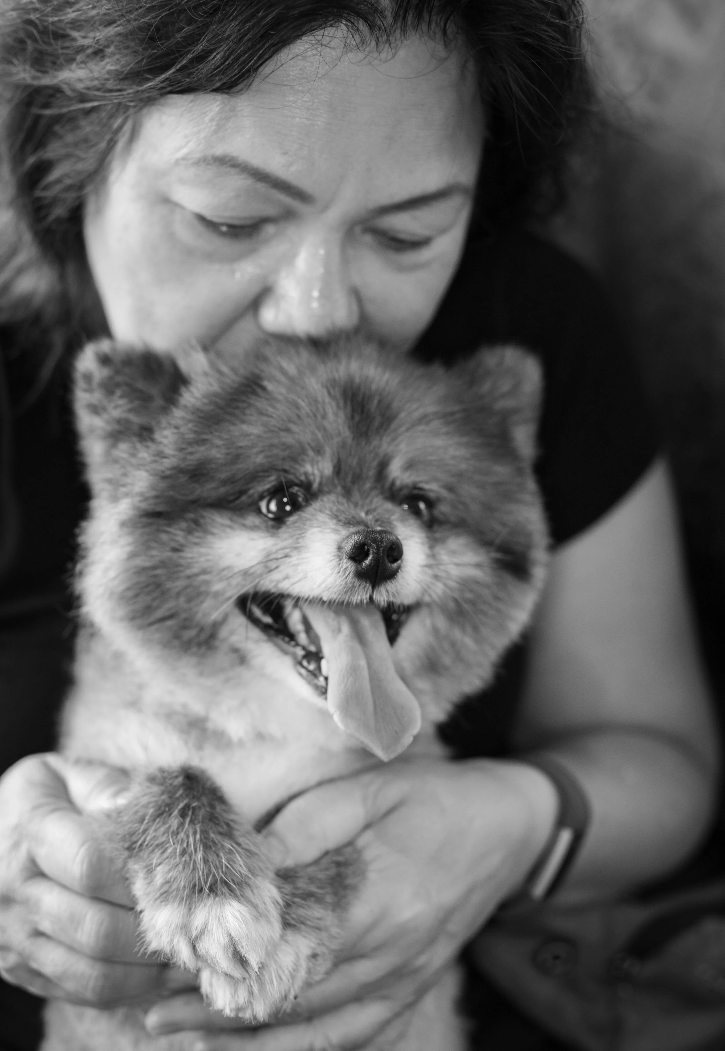 A woman hugging a cheerful, fluffy dog with its tongue out.