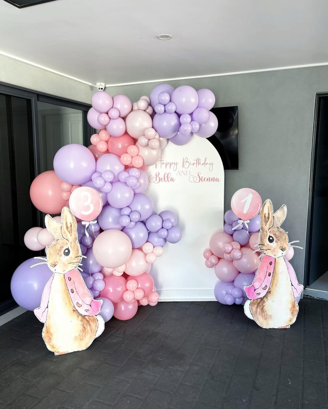 Decorative balloon arrangement with pastel purple and pink balloons, bunny cutouts, and birthday signs for Bella and Sienna's party.