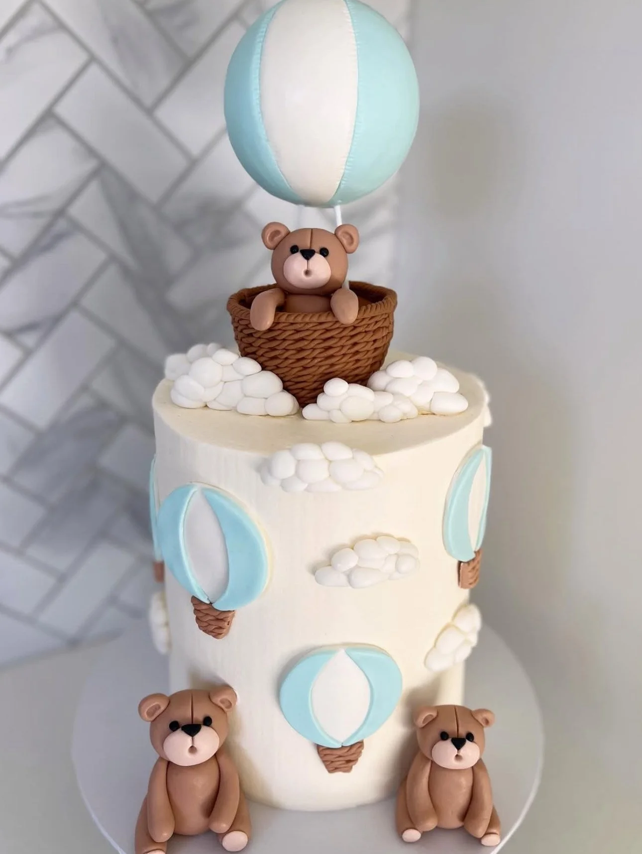 A cake decorated with teddy bears, hot air balloons, clouds, and a sky-blue and white hot air balloon on top.