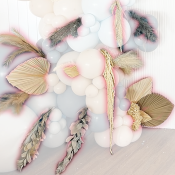 Decorative arrangement of white, pastel purple, and pink balloons with dried leaves and pampas grass accents.