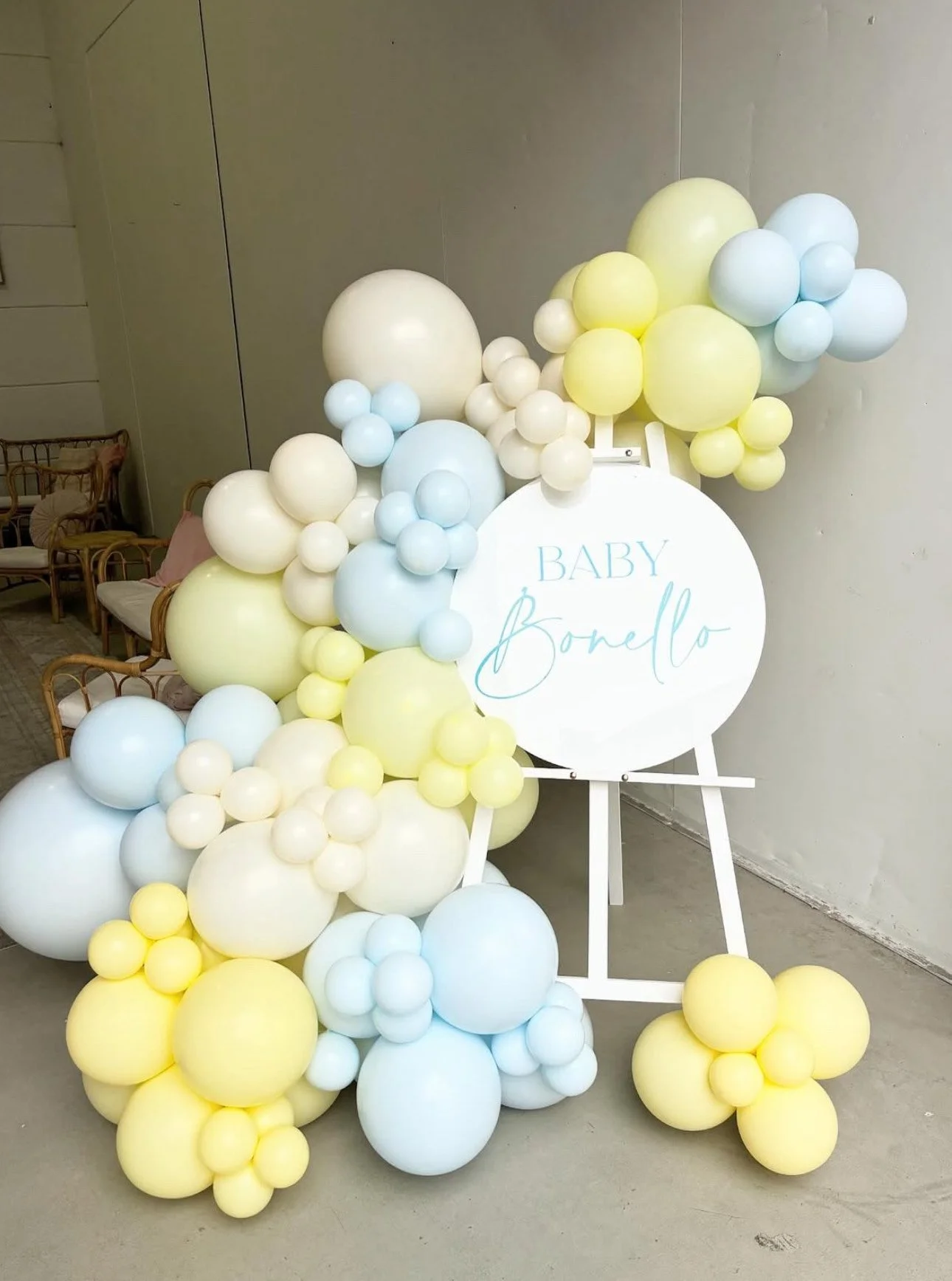 Baby bump photo display with pastel blue, yellow, and white balloons surrounding a white sign that reads 'Baby Bonello'