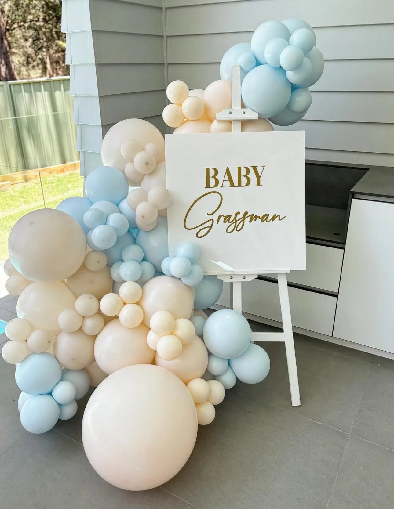 Balloon arrangement with a white sign that reads "Baby Grassman" for a celebration or baby shower.
