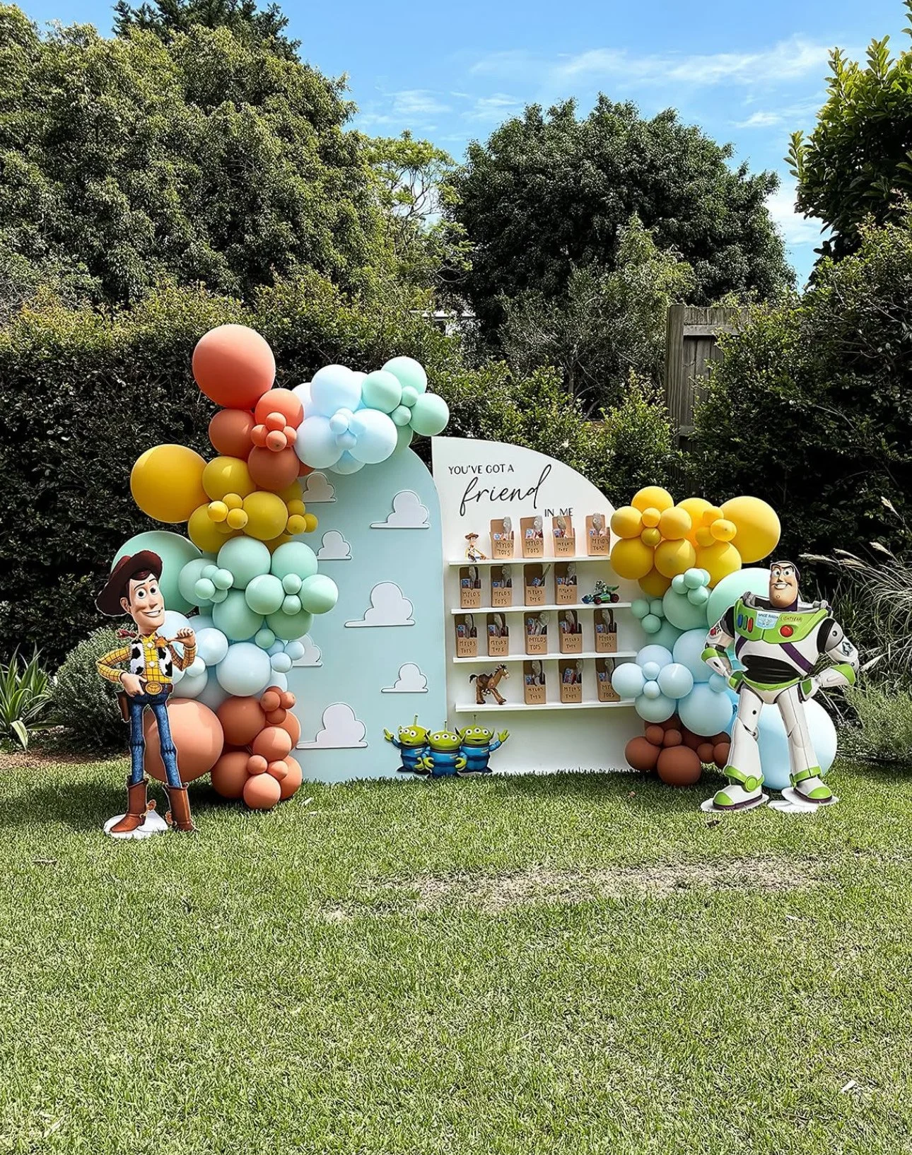 Toy Story-themed outdoor party display with balloons, Woody and Buzz Lightyear cutouts, and a white cloud-shaped backdrop with shelves of treats and decorations.