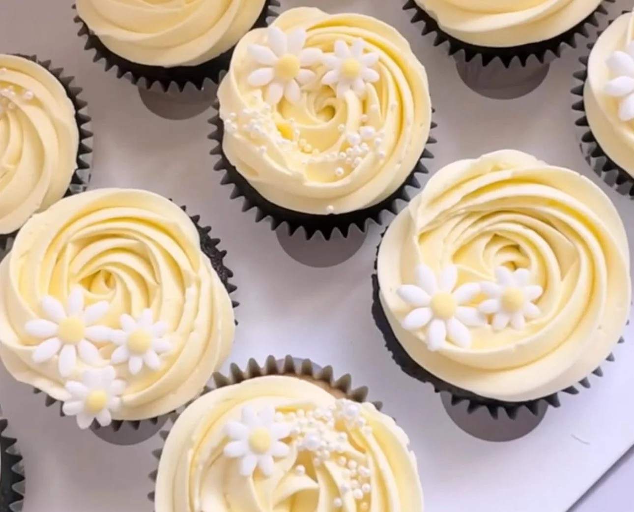 Cupcakes with pale yellow frosting decorated with small white and yellow flowers and white sprinkles.