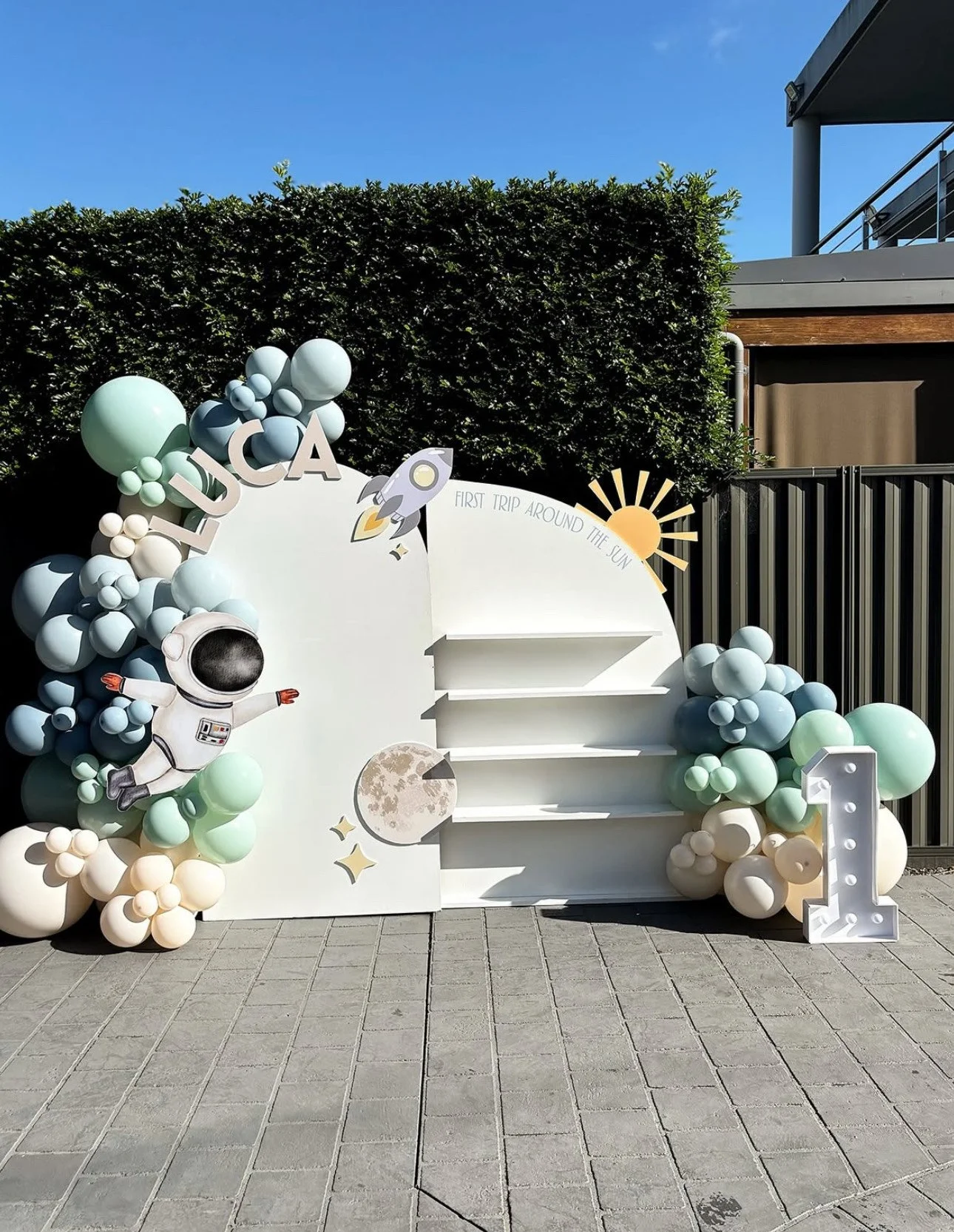 Space-themed birthday display with balloons, an astronaut figure, a rocket graphic, moon, sun, and the words 'LUCIA' and 'First Trip Around the Sun'.