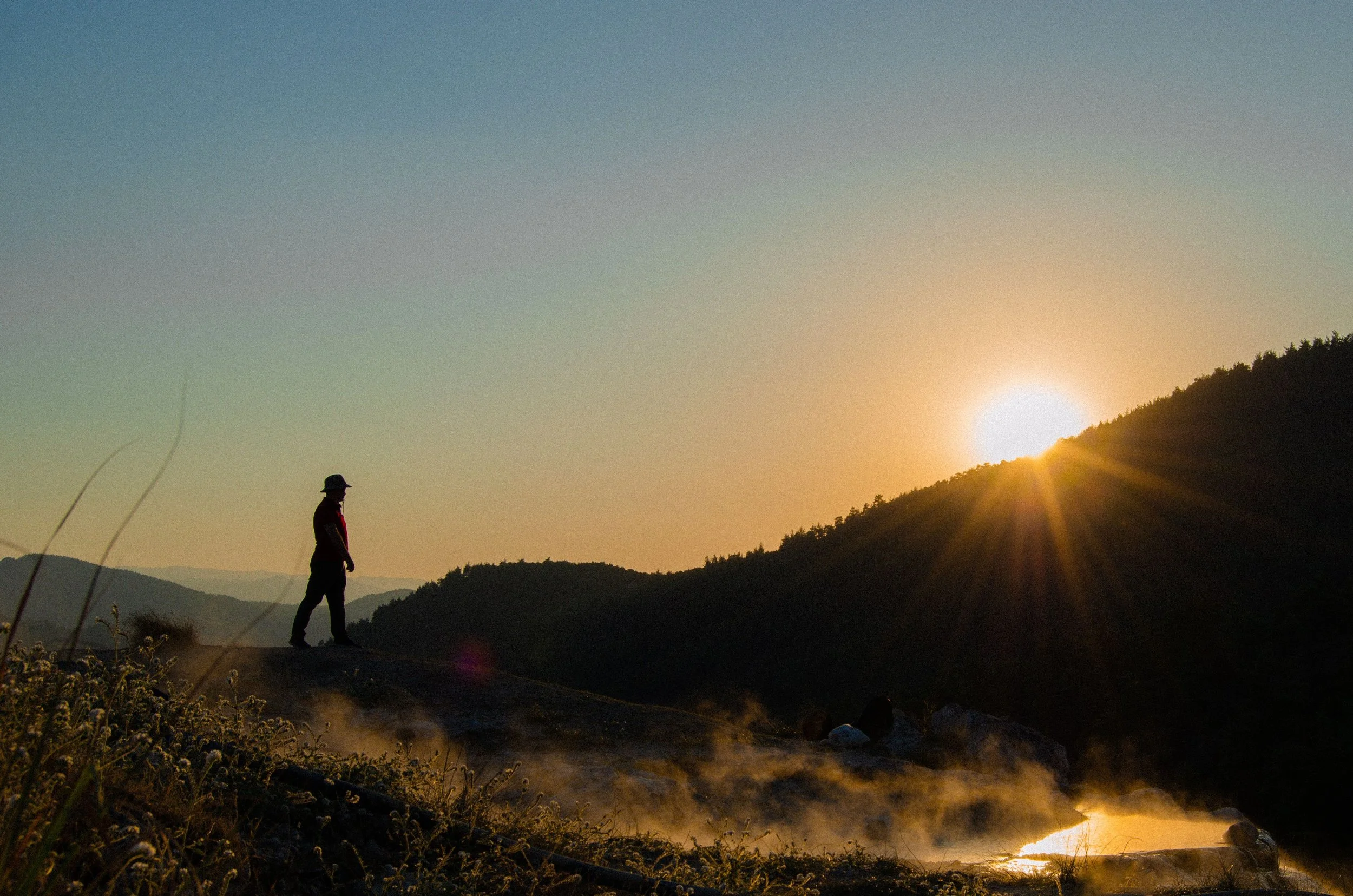 Person walking toward sunrise on a mountain trail, representing hope and healing in PTSD therapy