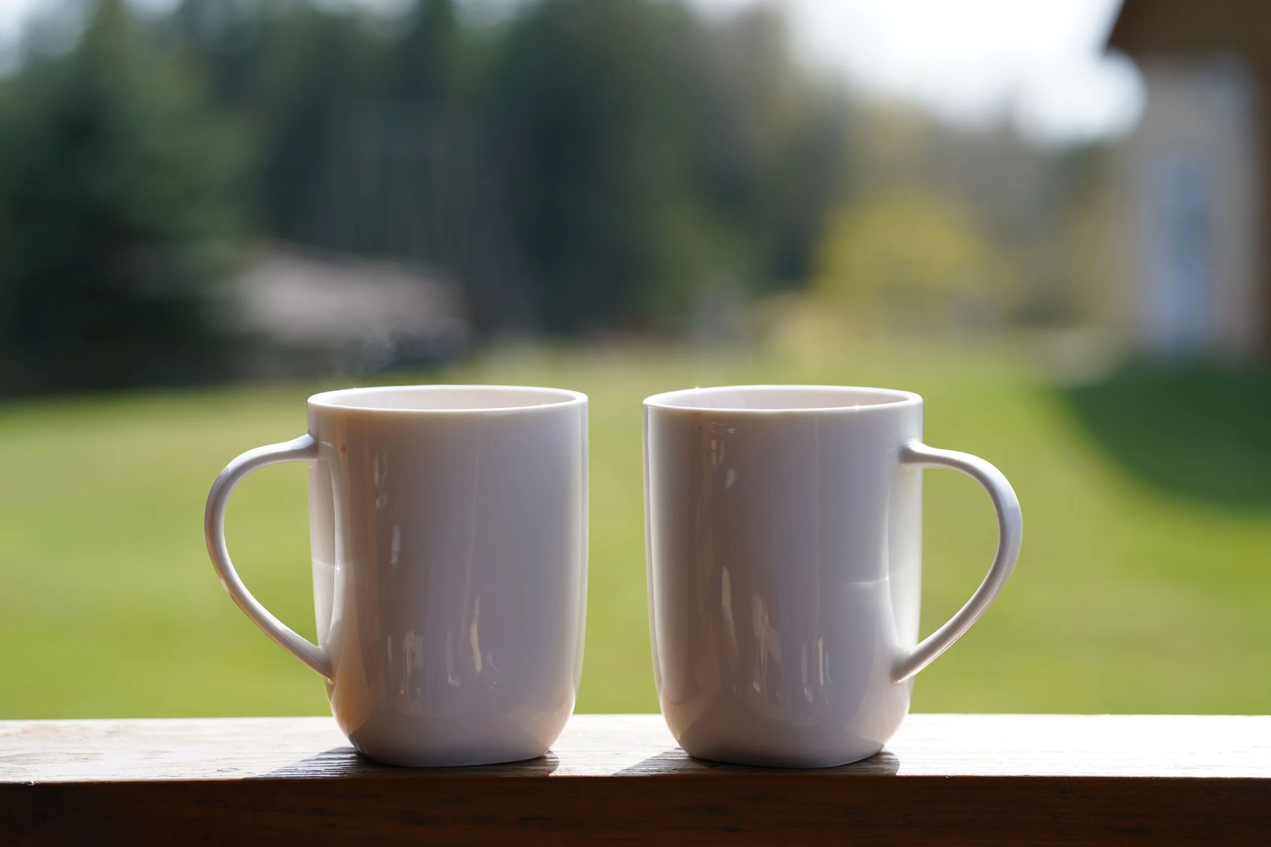 Two coffee cups rest on a windowsill with soft blurred greenery in the background, representing the quiet longing for connection that brings couples to Relational Life Therapy in Austin.