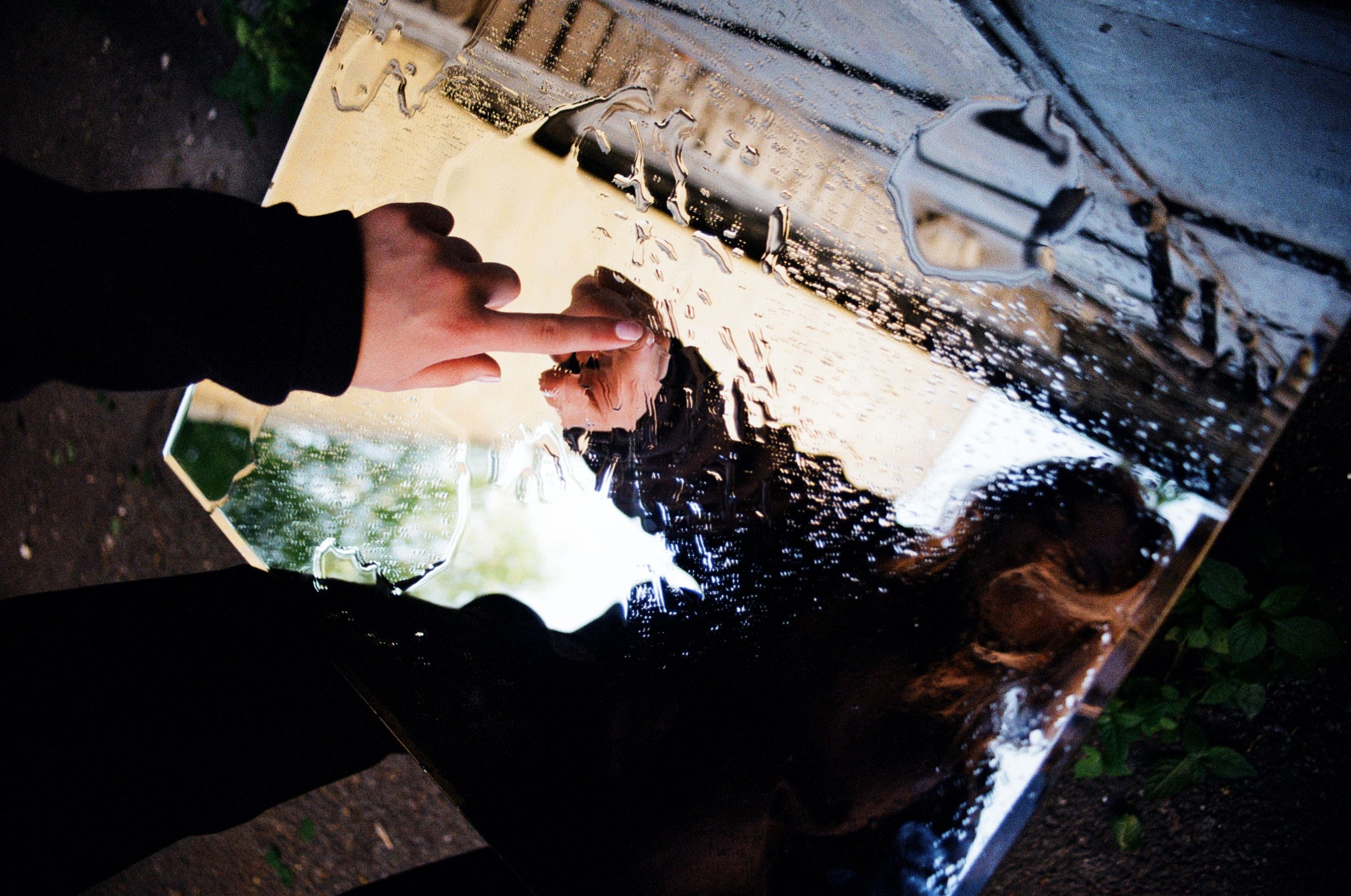 A hand pressed against a wet glass panel reflecting a distorted face, representing the loss of self and identity that can result from narcissistic abuse and emotional manipulation
