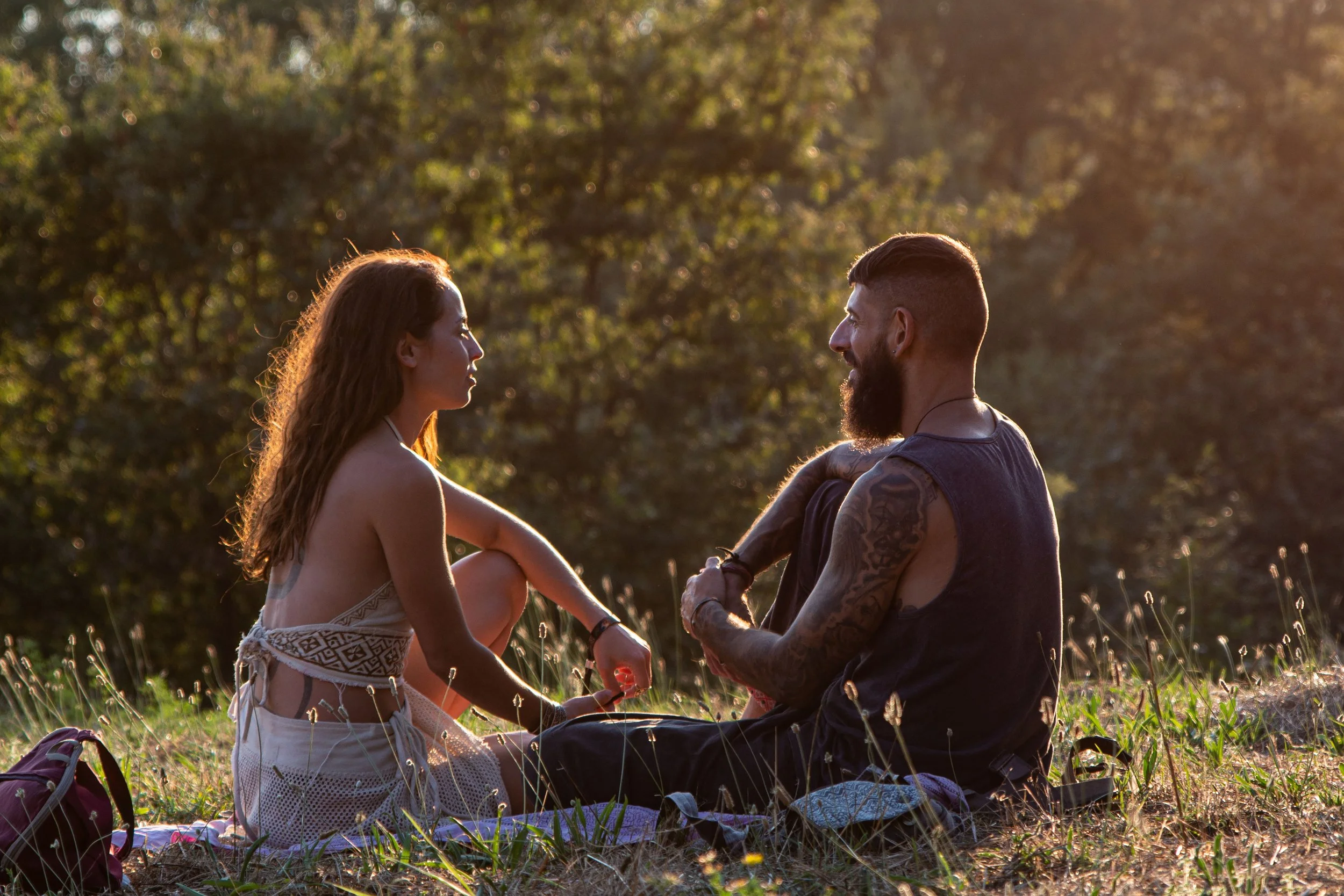A couple sitting on a blanket in a sunny glade, facing each other in deep conversation, representing the genuine human connection that AI and digital intimacy therapy can help restore.