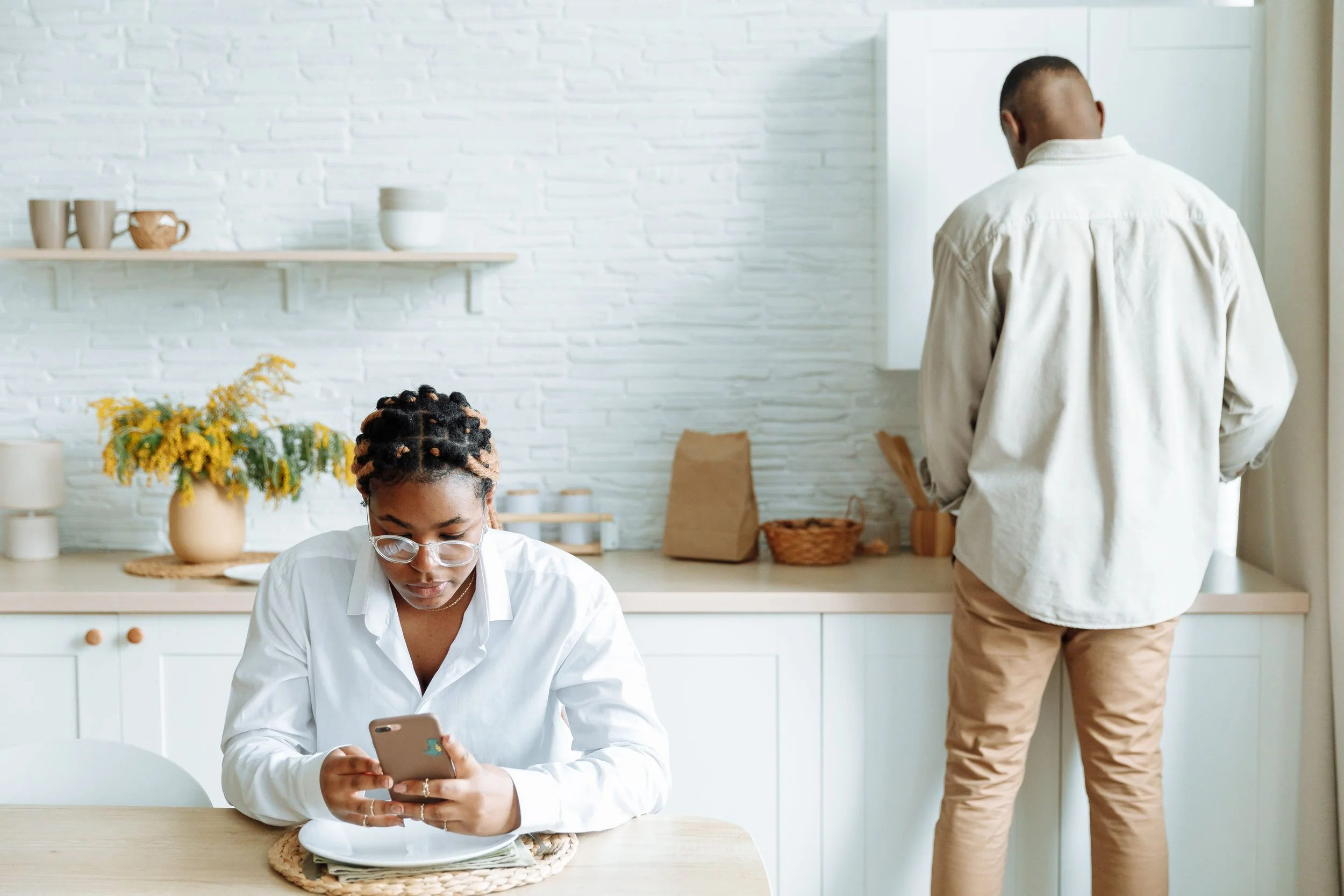 Couple navigating an empty nest transition, with one partner on the phone while the other does a household chore
