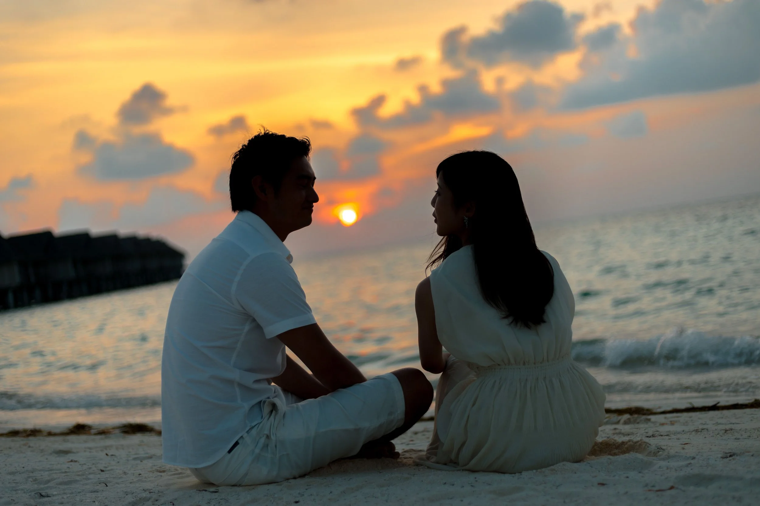 A couple sitting near each other in silhouette at dusk on the beach, representing the hope and possibility of reconnection through Gottman Method couples therapy in Austin, TX.