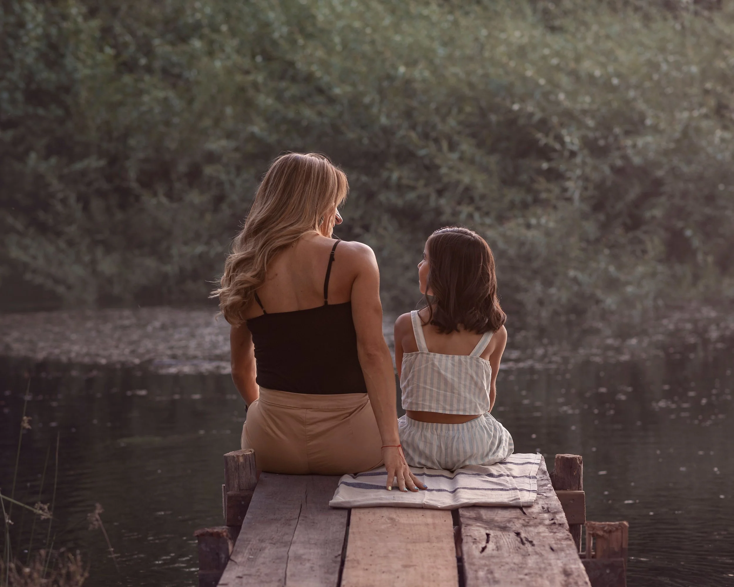 A mother and daughter spend a quiet moment together by the water. When mothers begin to understand and heal the patterns they inherited, they can create a different emotional environment for themselves and their children.