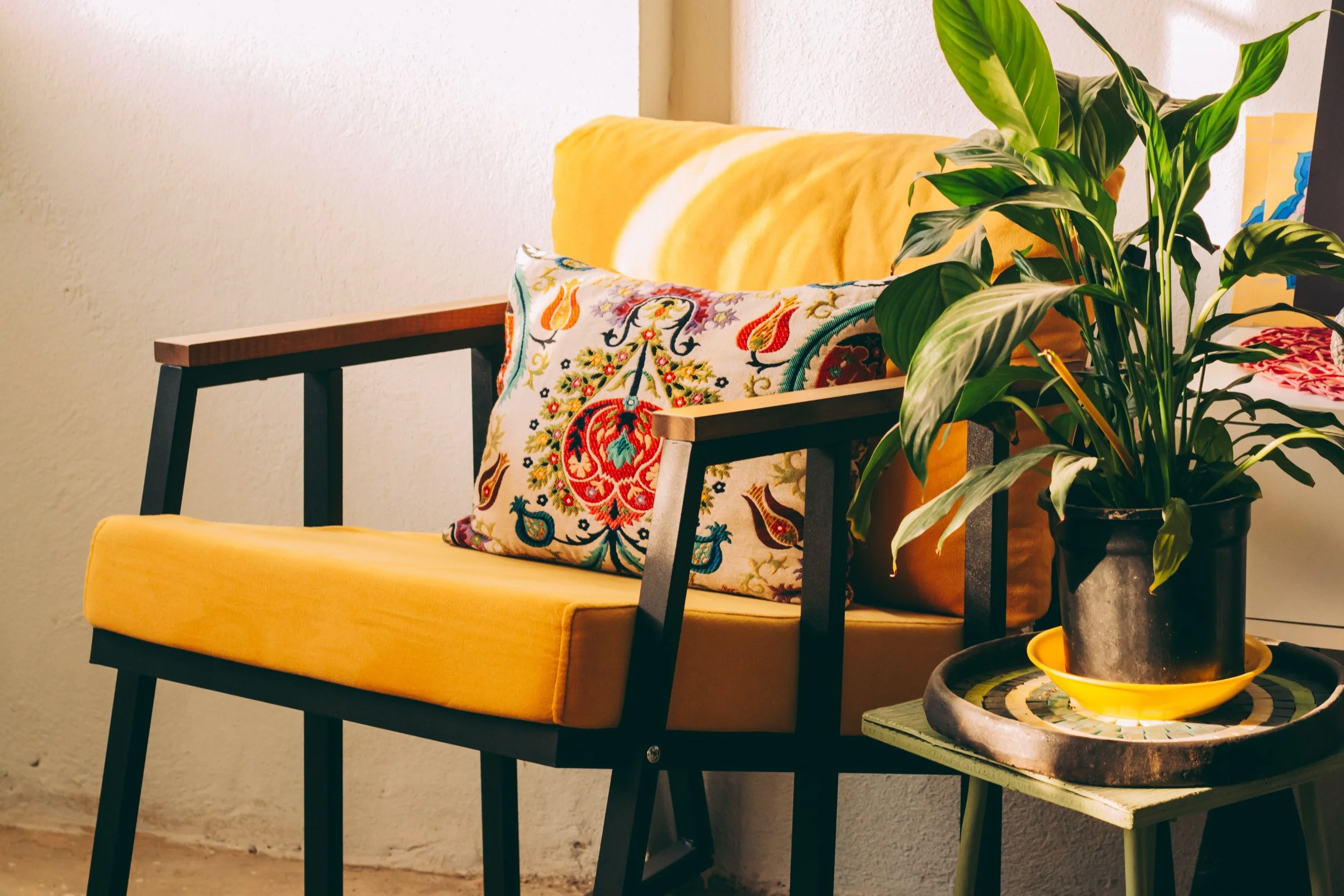 A cozy yellow chair with a colorful throw pillow beside a small table with a plant, representing the warmth and safety of the therapy space at Seek the Sun Psychotherapy.