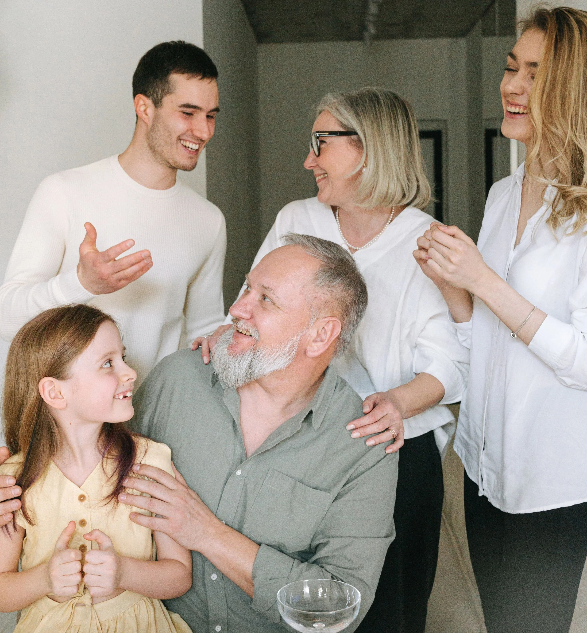 A multigenerational family gathered around a grandfather at a dinner table with a young child in his lap and family members exchanging warm looks, representing the family dynamics that empty nest couples navigate alongside their relationship
