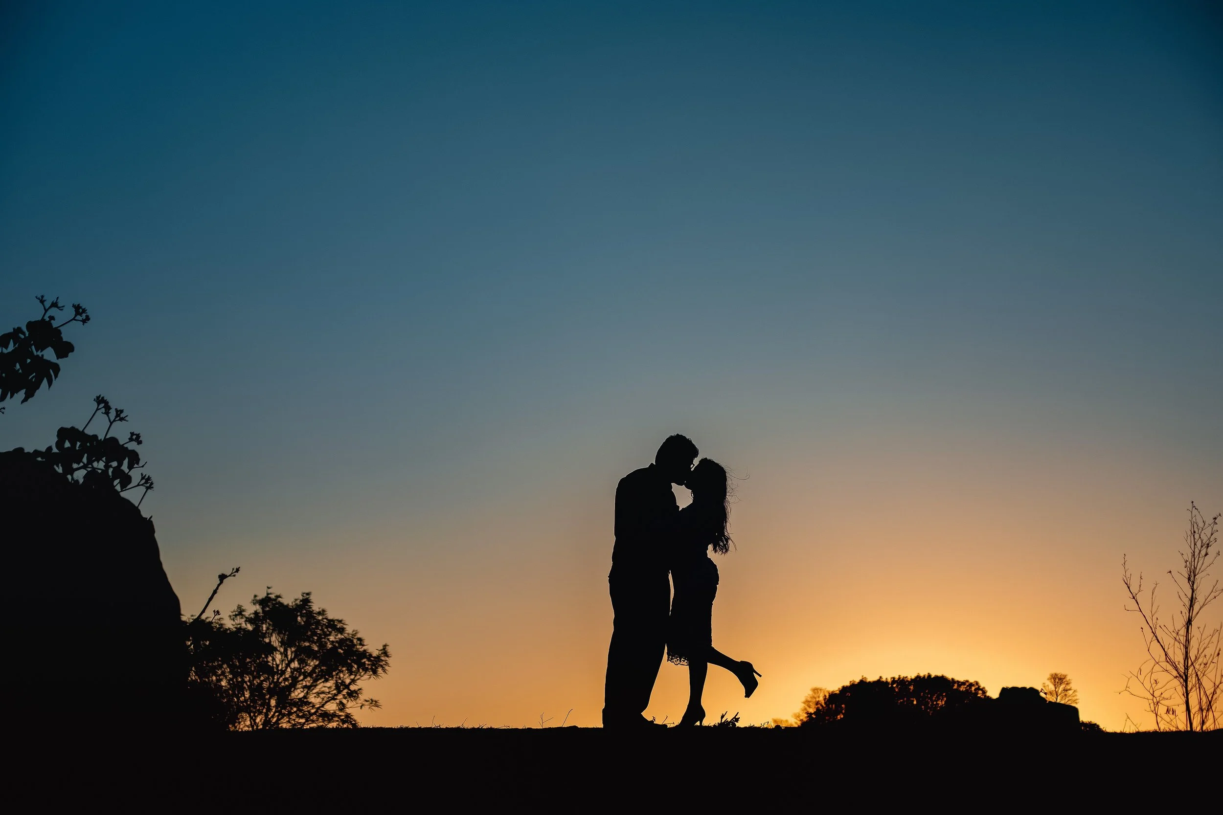 A silhouetted couple sharing a kiss outdoors at sunset, representing the emotional connection and intimacy that trauma-informed couples therapy can help restore
