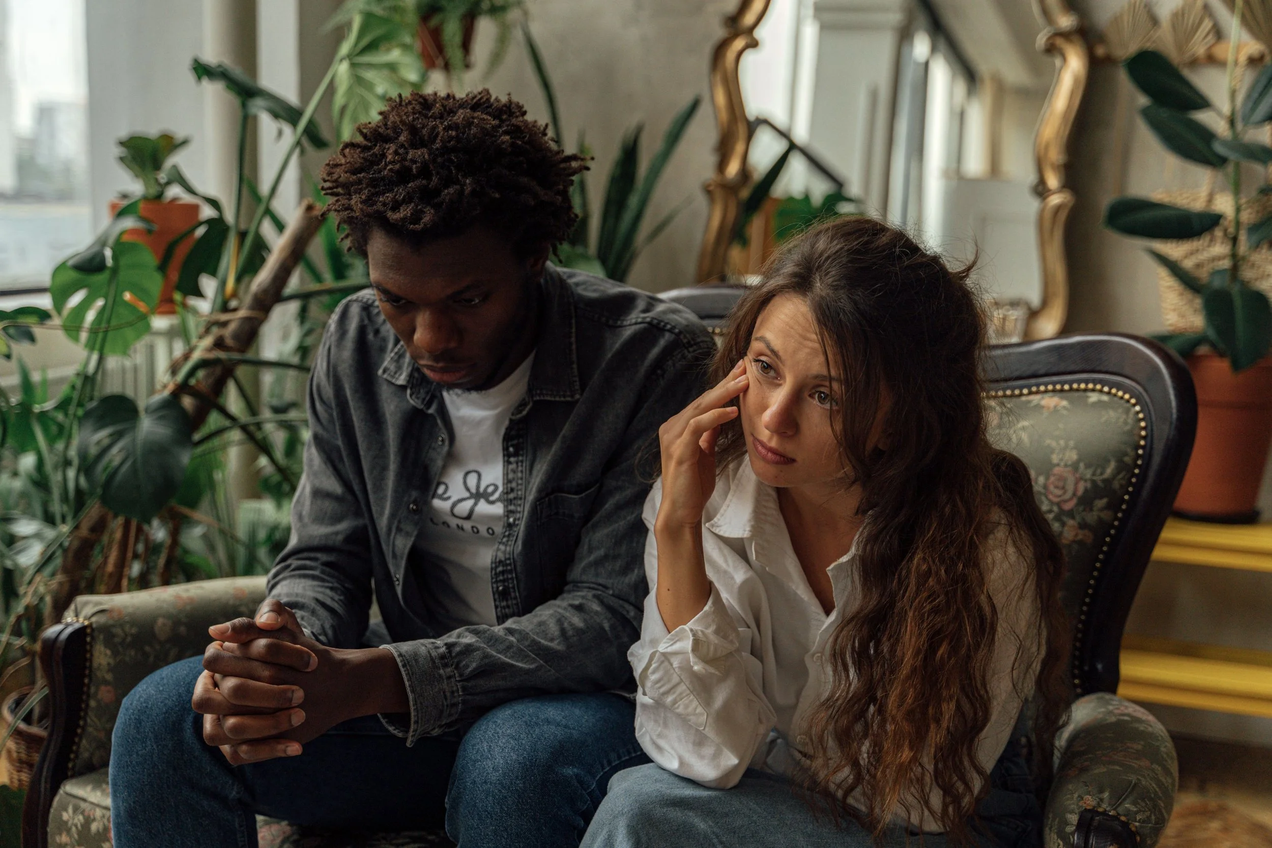 Couple sitting together on a couch in a plant-filled room, reflecting and reconnecting during Gottman Method couples therapy
