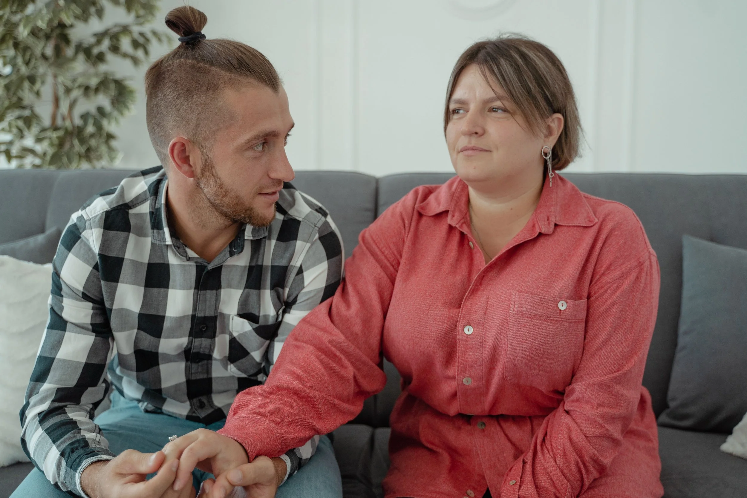 A couple in a Gottman therapy session in Austin Texas, a man turned toward his partner holding her hand on a couch.
