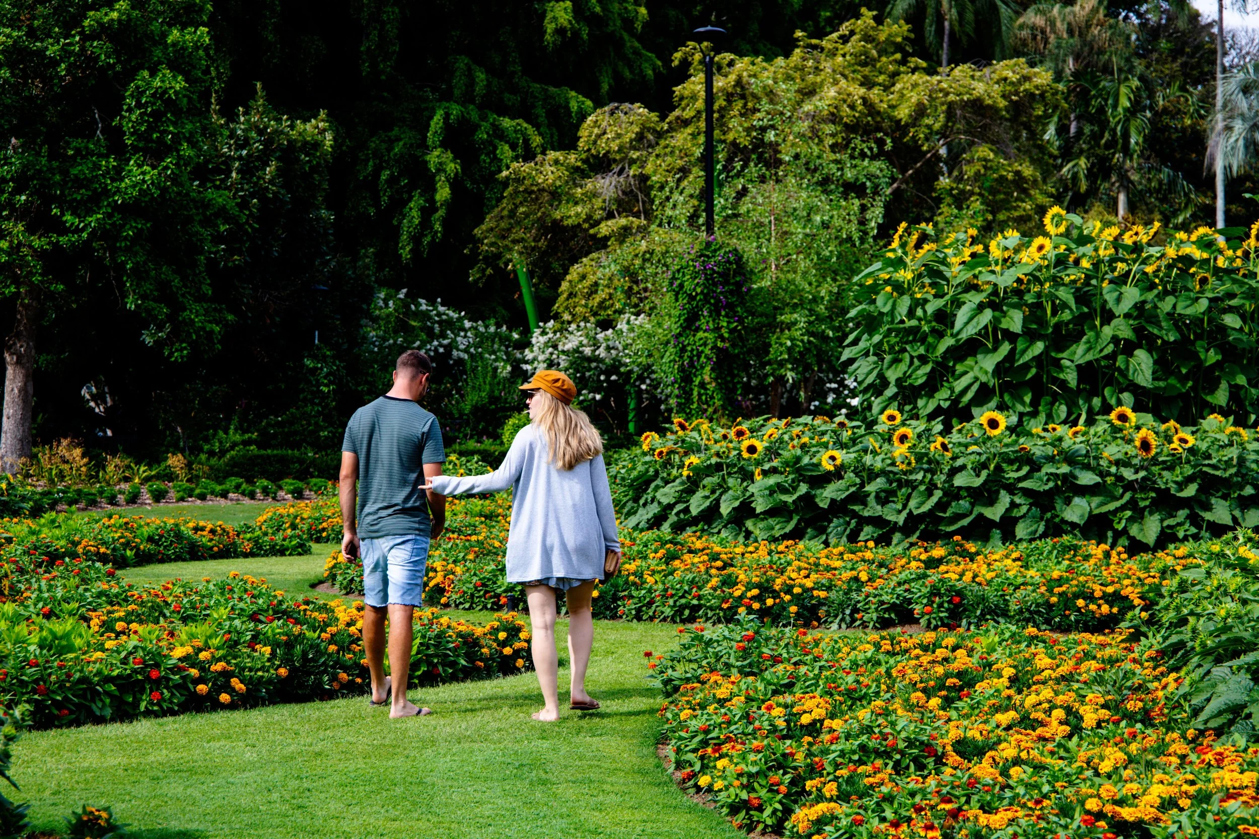 A couple walks through a sunflower garden; she points toward something in the distance while he looks down, capturing the ongoing work of finding connection in a relationship.