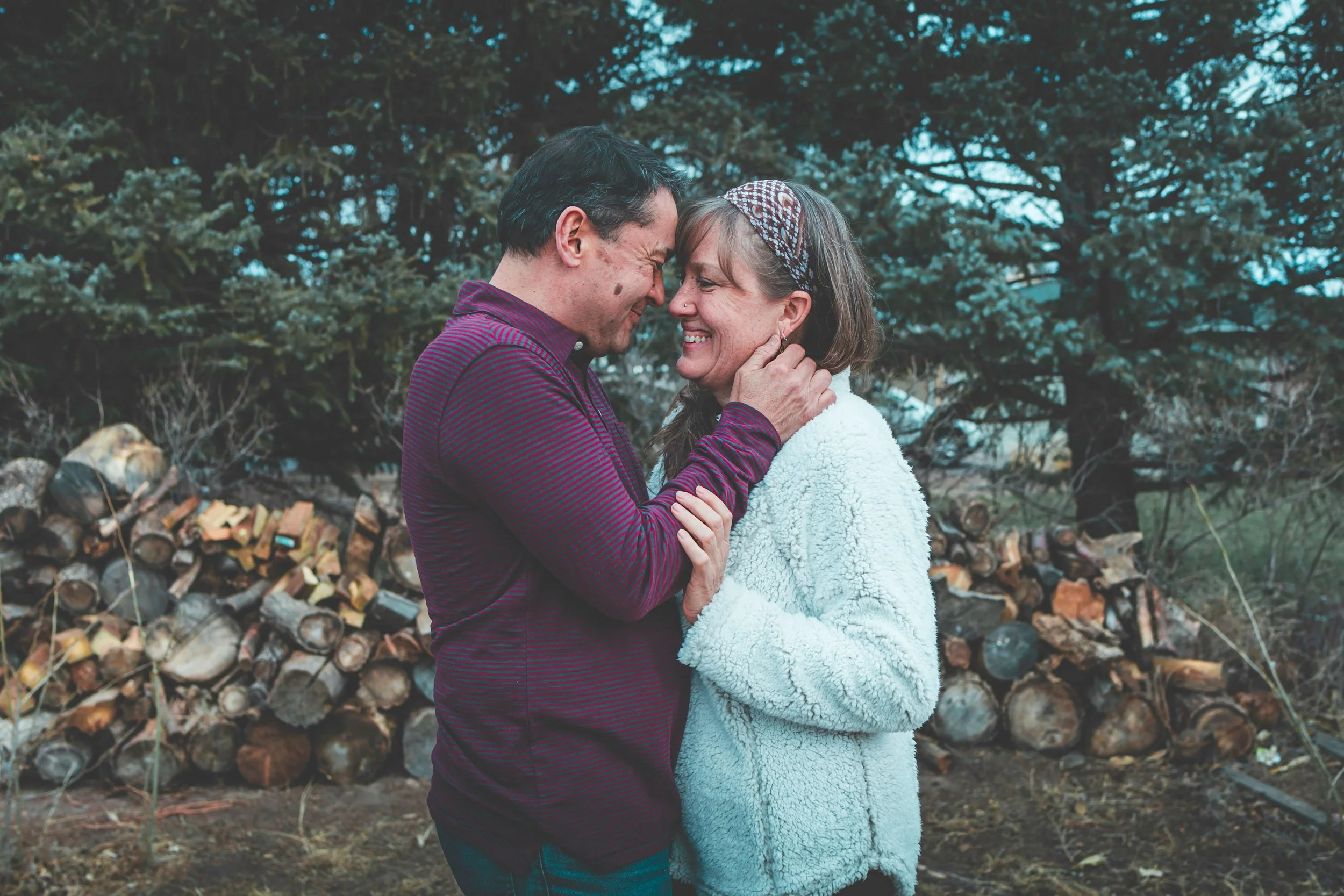 A couple  touching foreheads and smiling against a wooden backdrop, representing the tenderness and reconnection that empty nest couples therapy can make possible