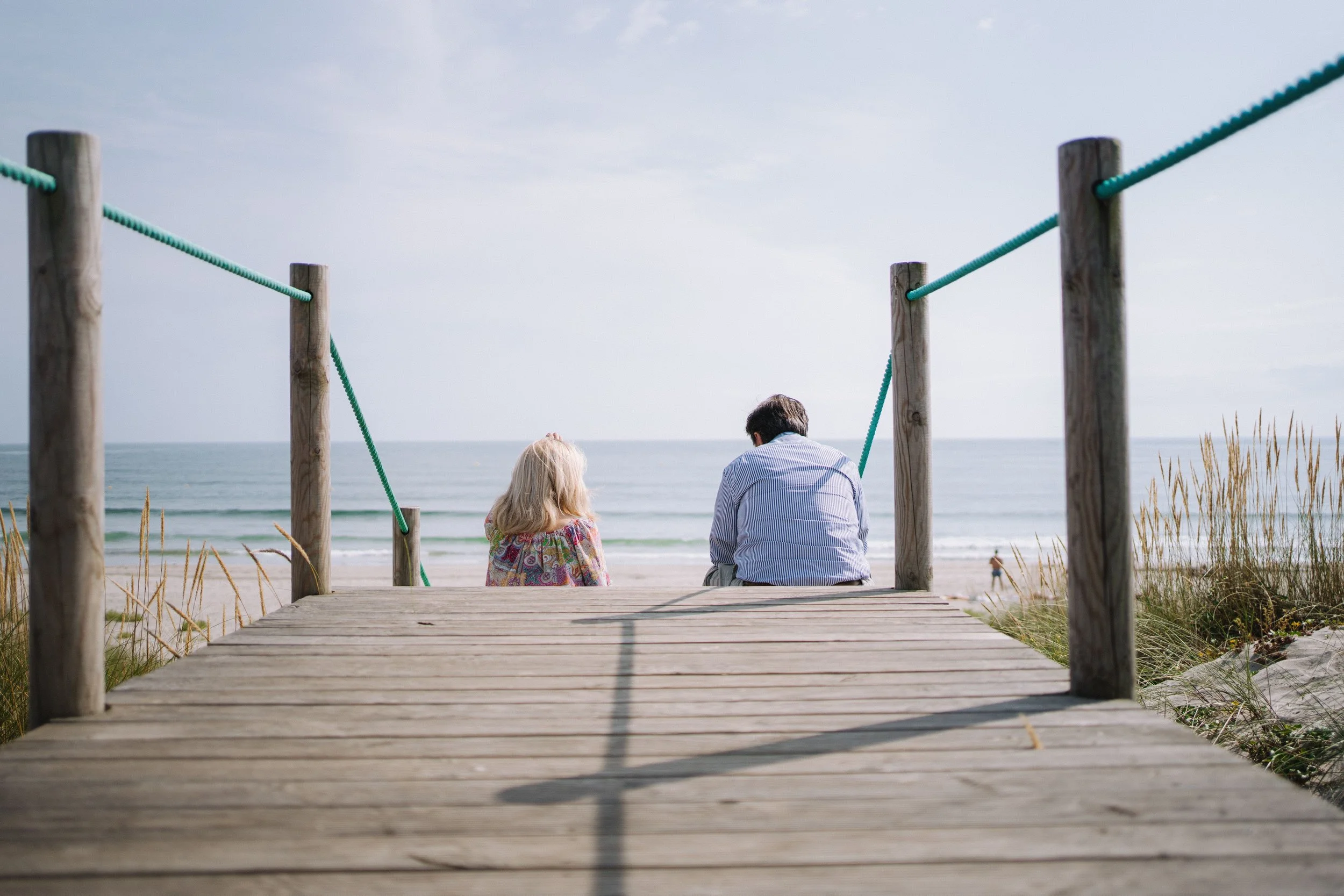 A couple sitting apart at the end of a trail overlooking the beach, representing the distance and hope that brings couples to Gottman Method therapy in Austin, TX.