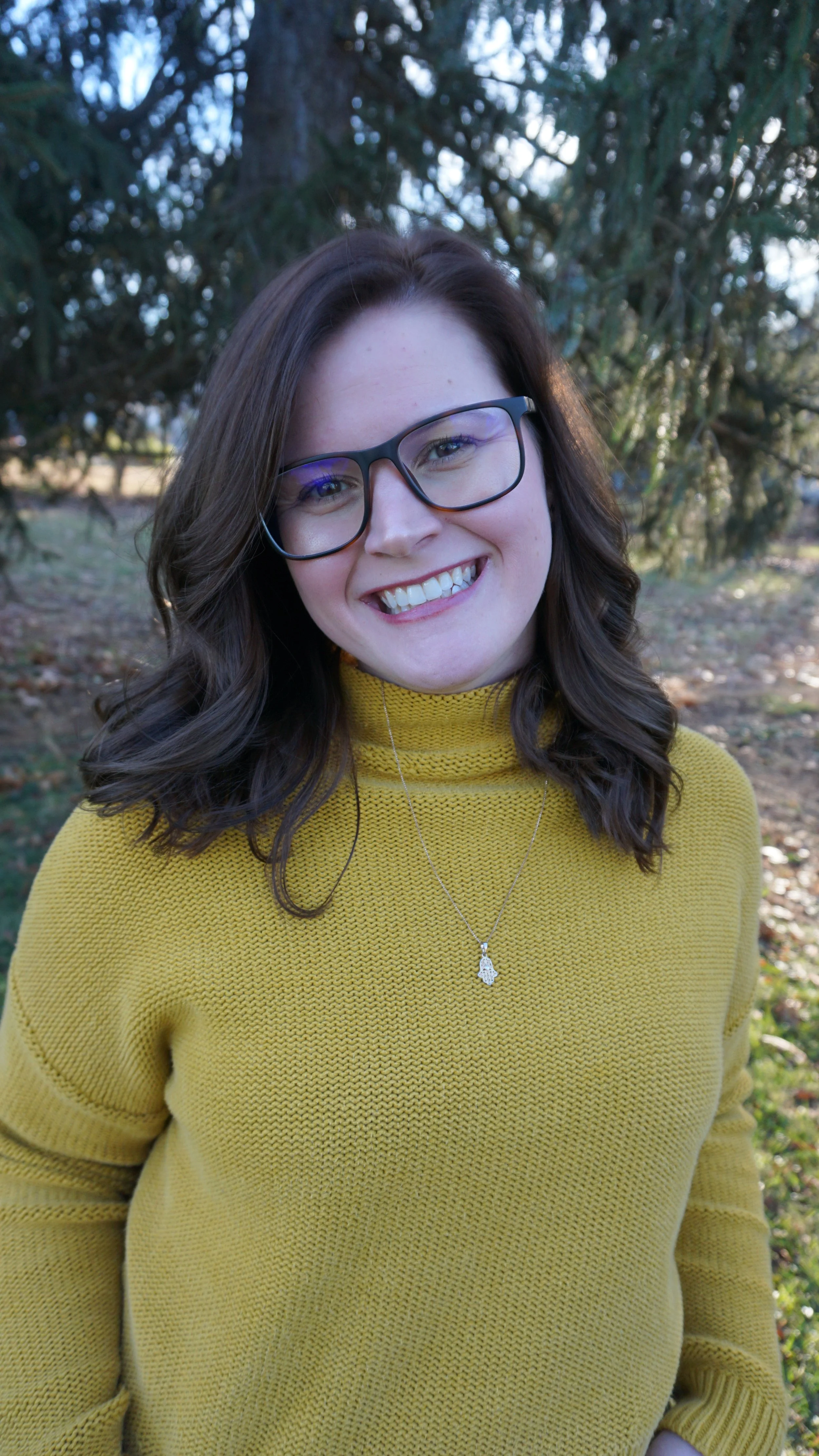Woman in glasses stands in front of tree smiling