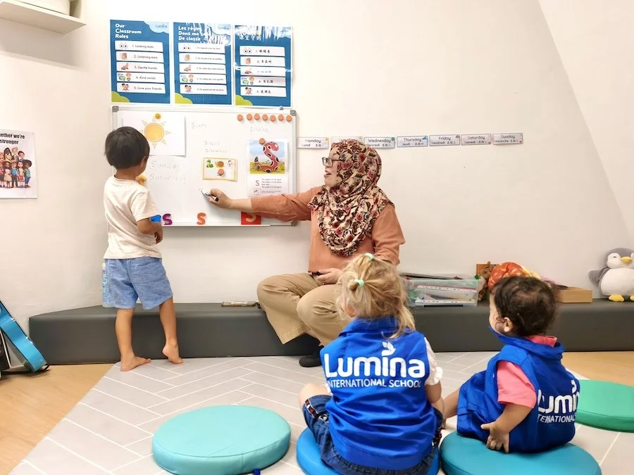 Two young boys dressed in business suits and large glasses sit at a cluttered desk, expressing frustration as colorful sticky notes are falling and stuck to their foreheads, with a calculator, notepad, and clock on the desk.