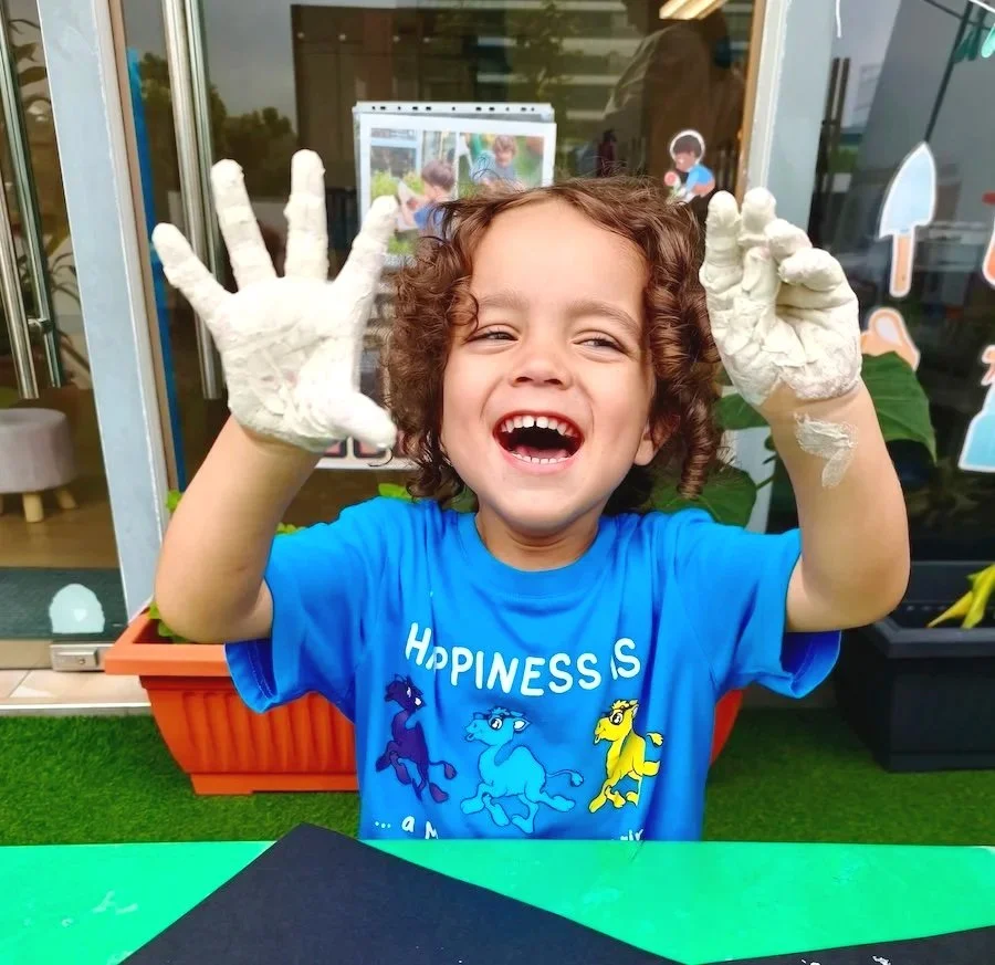 Two young girls playing with bubbles outdoors on a sunny day, one with curly hair laughing and the other with straight hair blowing bubbles.