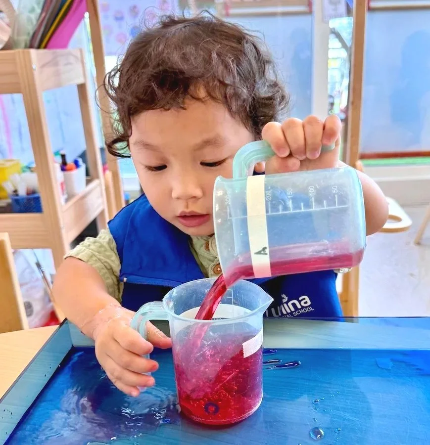 A young boy wearing safety goggles adjusting them with both hands, wearing a white shirt with printed text.